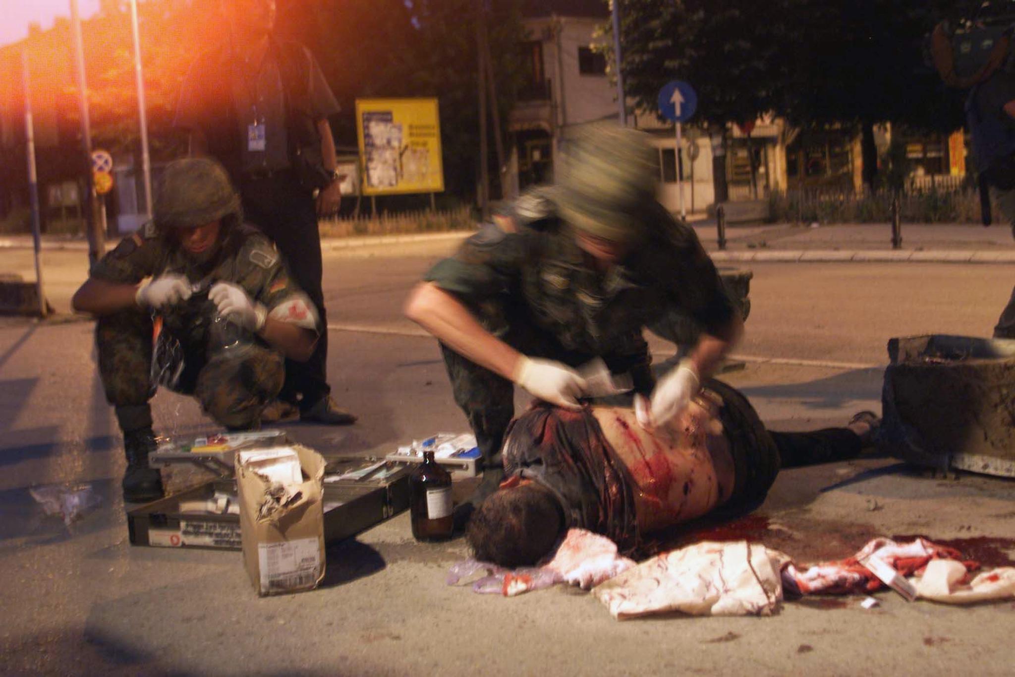 An injured Serbian sniper lies on the ground as German military doctors try to treat him in Prizren, 13 June 1999