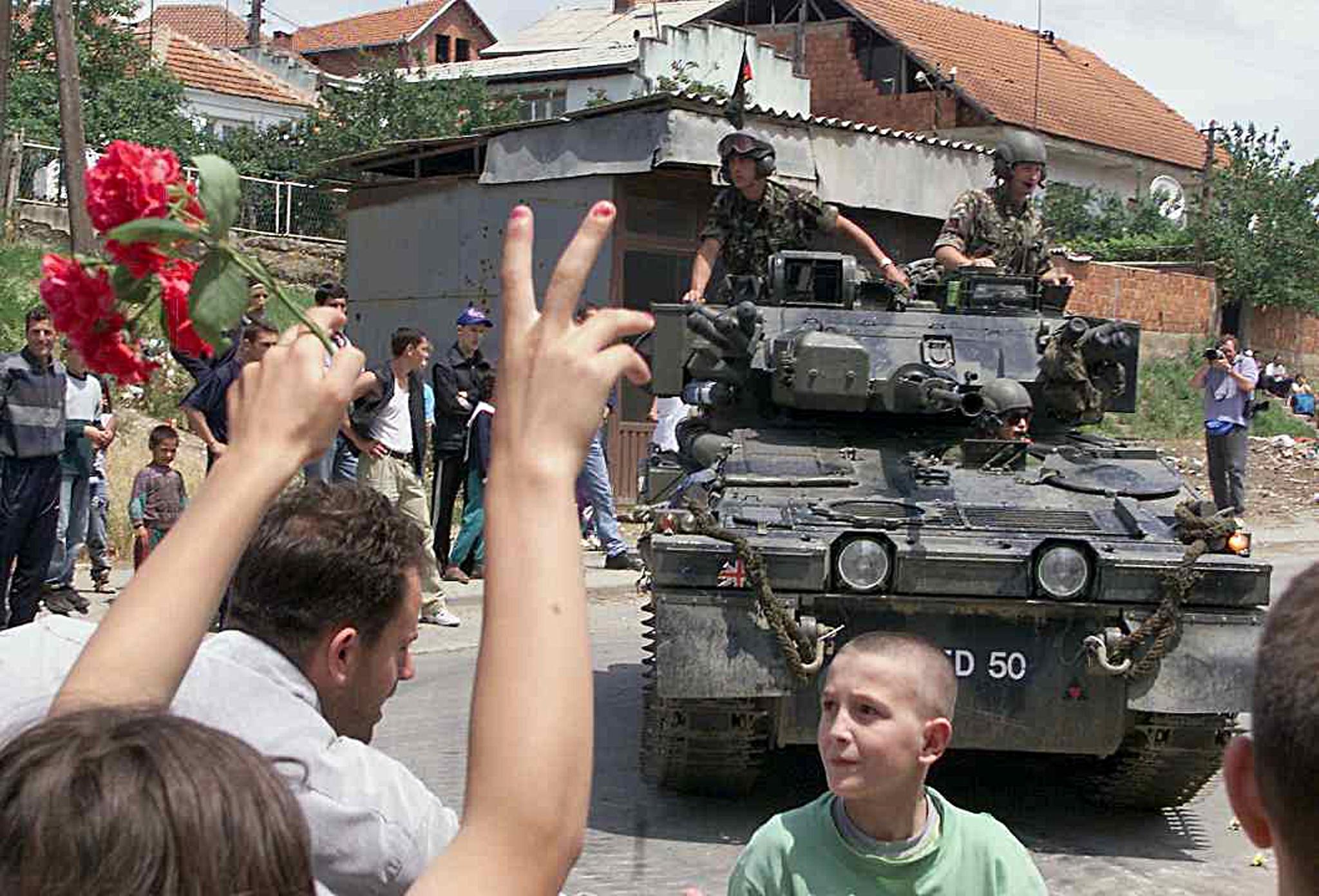 Ethnic Albanian people flash the victory sign and celebrate in front of a British Nato tank, its gun barrel decorated with flowers, as the first Nato troops are deployed in Kosovo’s capital Pristina, 13 June 1999