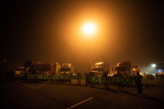 <p>Truckers and supporters raise their fists and hold a banner before a cross-country convoy destined for Ottawa to protest a federal vaccine mandate for truckers departed in Delta, British Columbia, Canada on Sunday, Jan. 23, 2022. </p>