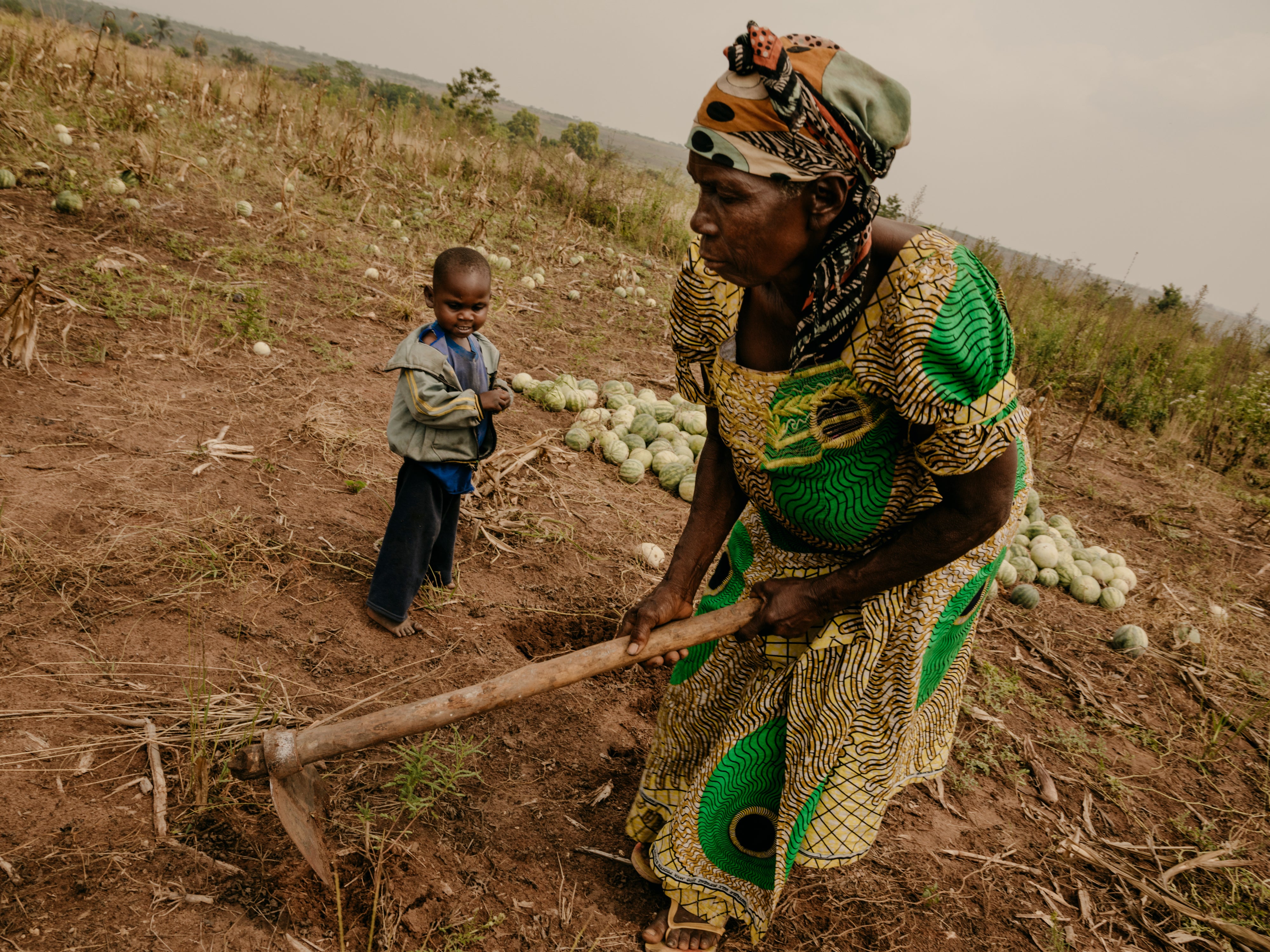 Jeannine*, 69, working on her crop field with her malnourished grandson Eriq*, 4