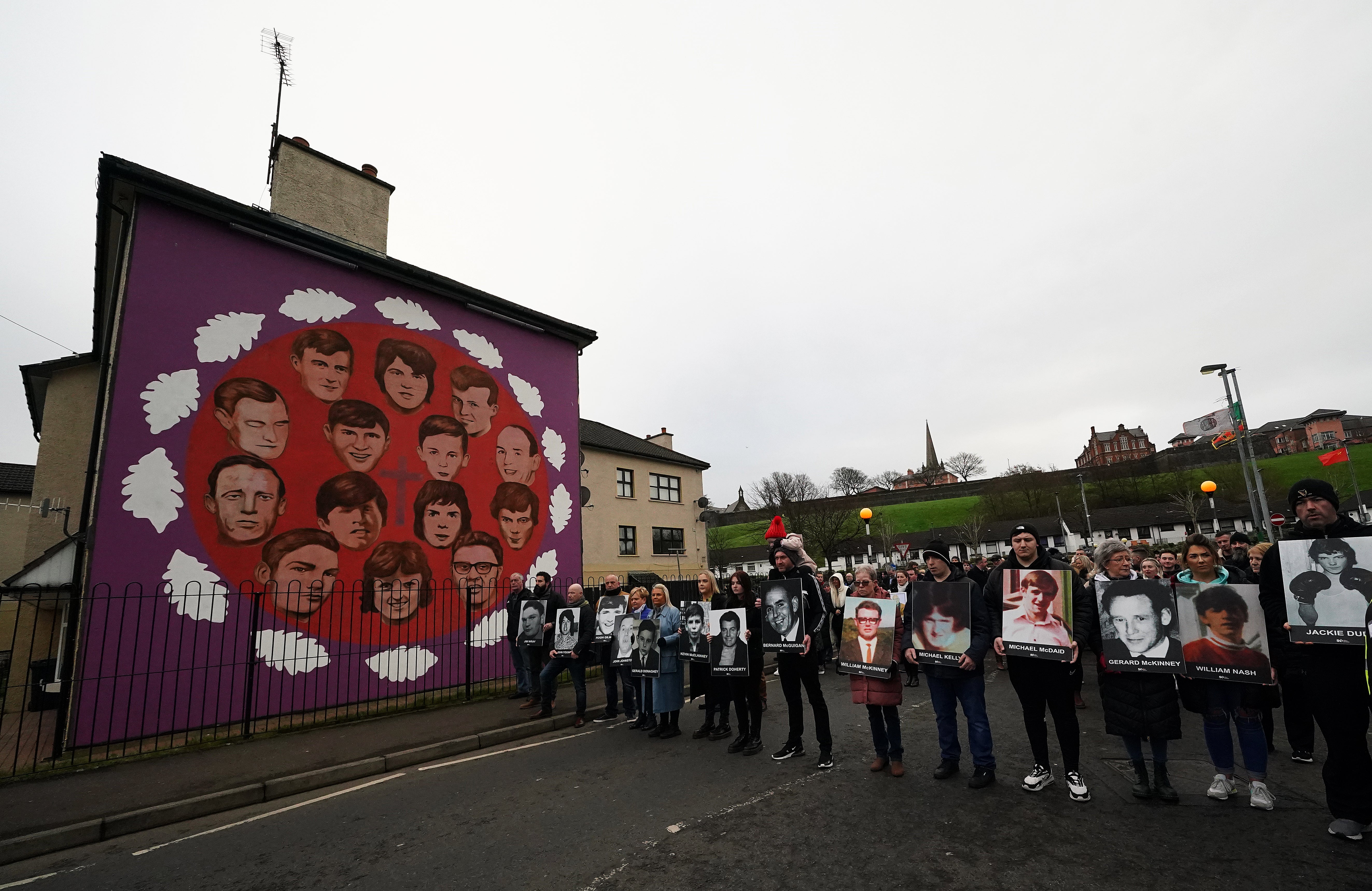 Family members holding photographs of the victims stop at a mural (Brian Lawless/PA)