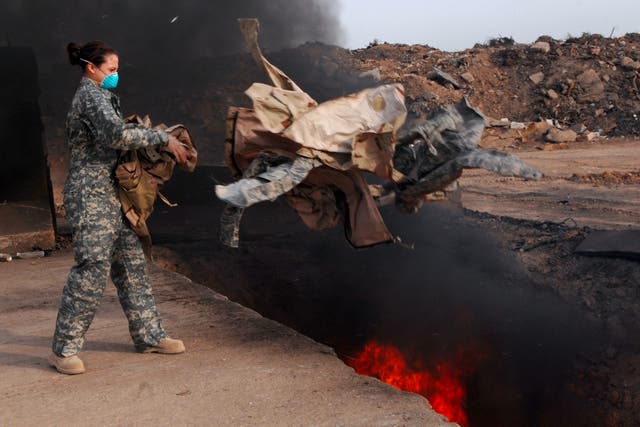 <p>A US servicemember tosses trash into a huge burn pit </p>