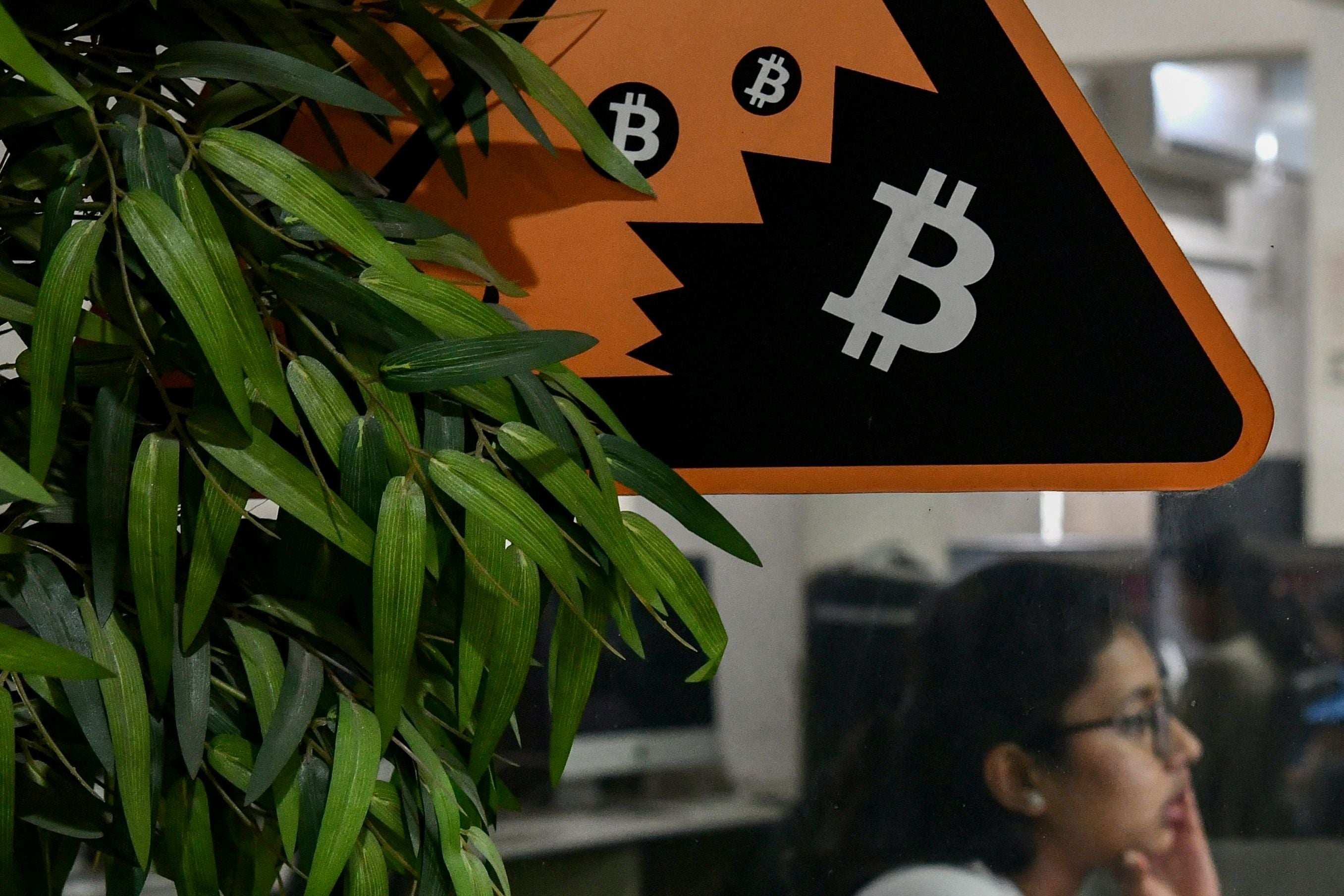 In this picture taken on November 23, 2021 an employee works on her workstation on the backdrop of the cryptocurrency symbol of Bitcoin pasted on a glass door of a private office in Bengaluru