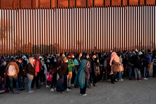 Migrantes que buscan asilo en EE. UU., en su mayoría de Venezuela, se paran cerca de la valla fronteriza mientras esperan ser procesados por la patrulla fronteriza de EE. UU. después de cruzar la frontera desde México en Yuma, Arizona.