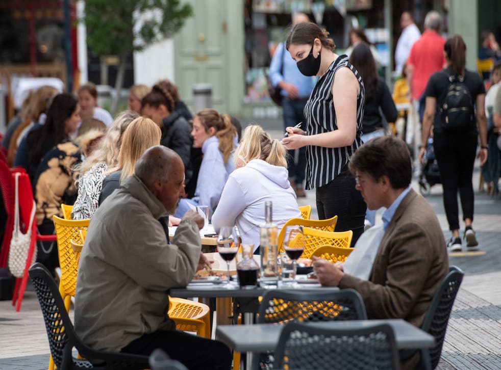 A waitress wearing a face covering serves diners at outside tables in Kensington, London. New data suggests it only takes two days after infection for first Covid symptoms to appear (PA)
