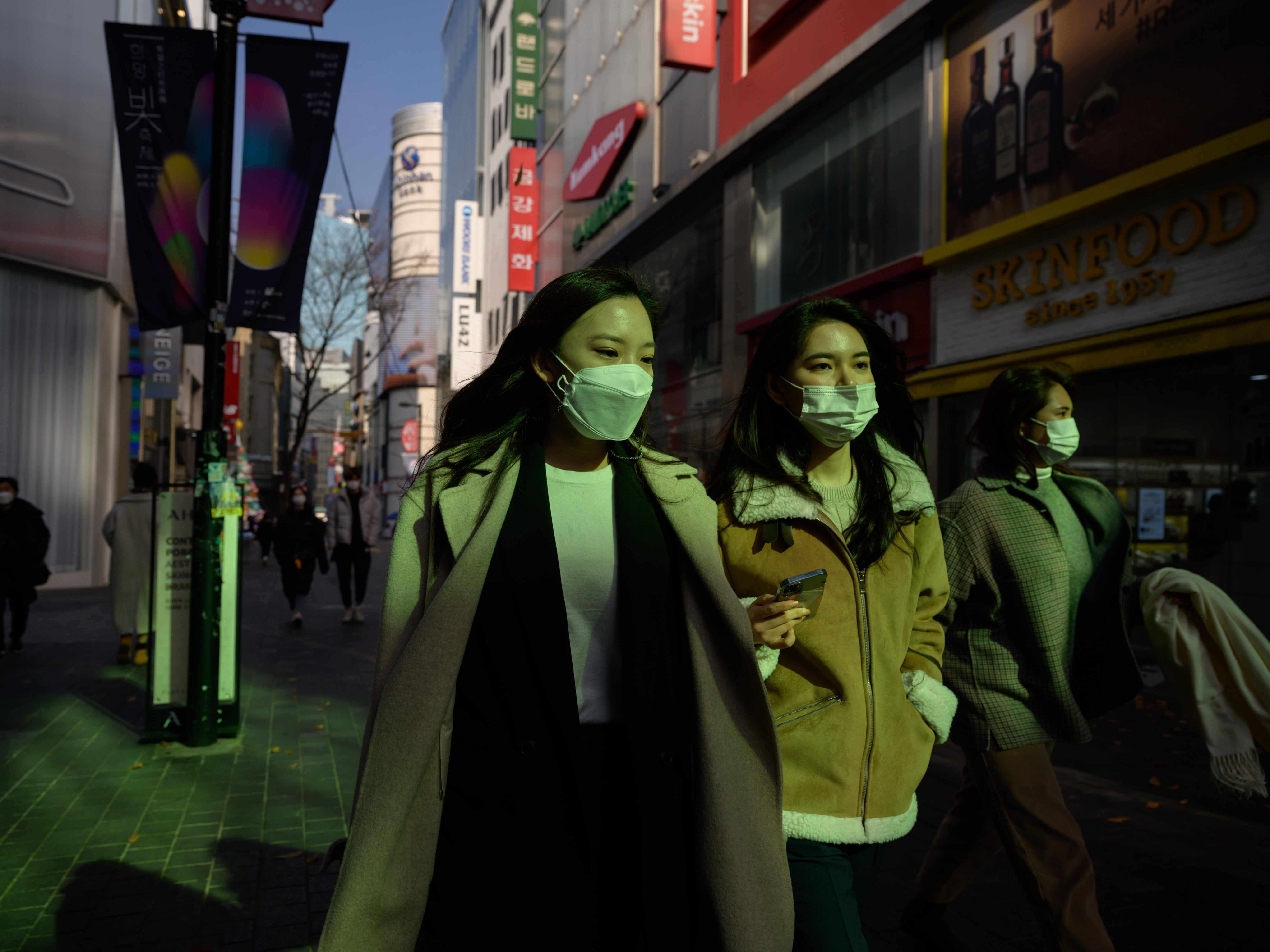 Shoppers wearing face masks walk through the Myeongdong shopping district of Seoul on November 26, 2020