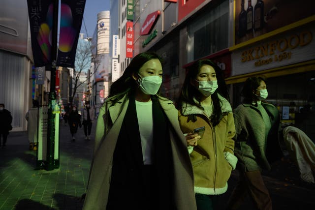 <p>Shoppers wearing face masks walk through the Myeongdong shopping district of Seoul on November 26, 2020</p>