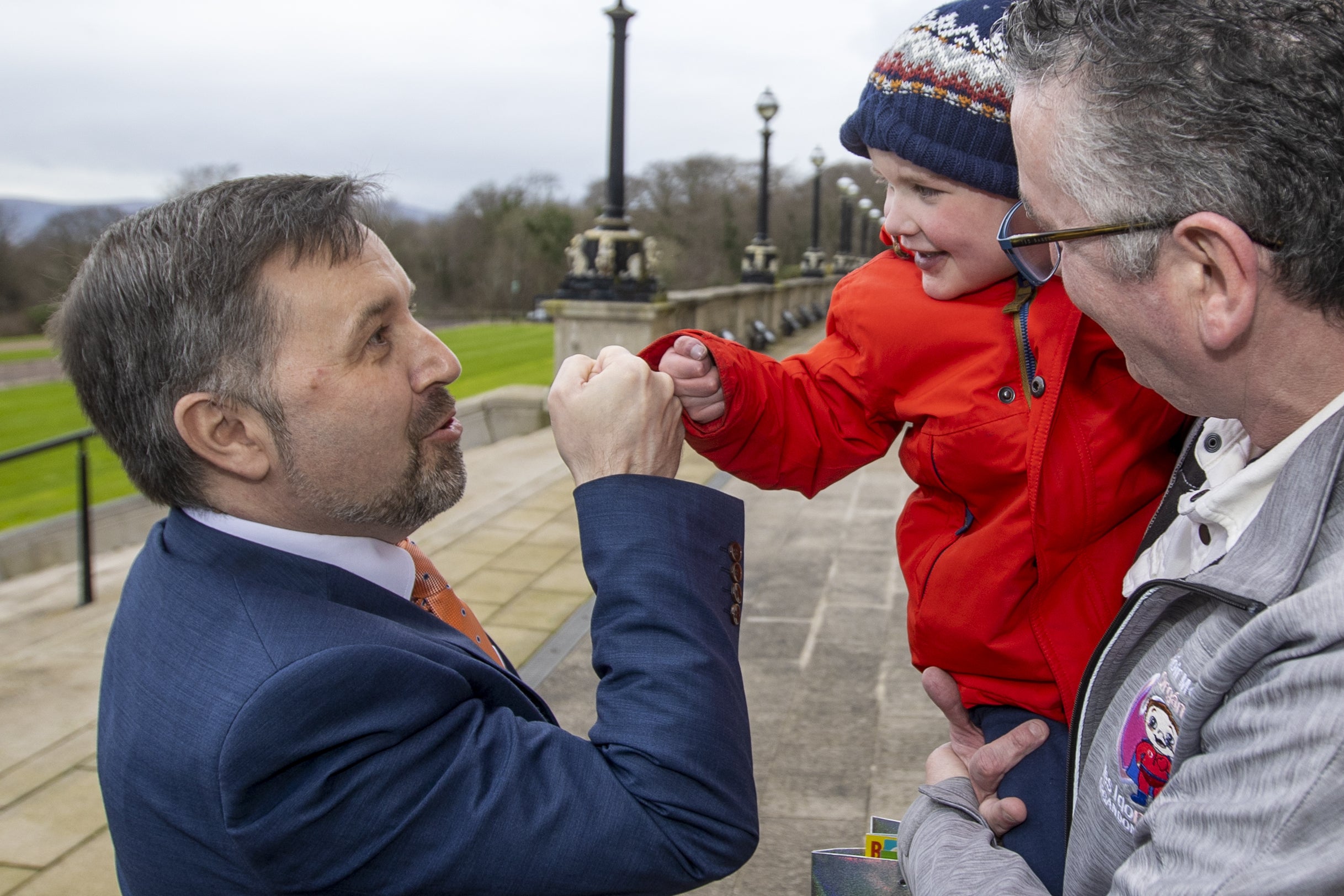 Health Minister Robin Swann fist bumps Daithi MacGabhann being held by his grandfather Martin Smith on the steps of Parliament Buildings at Stormont. (Liam McBurney/PA)