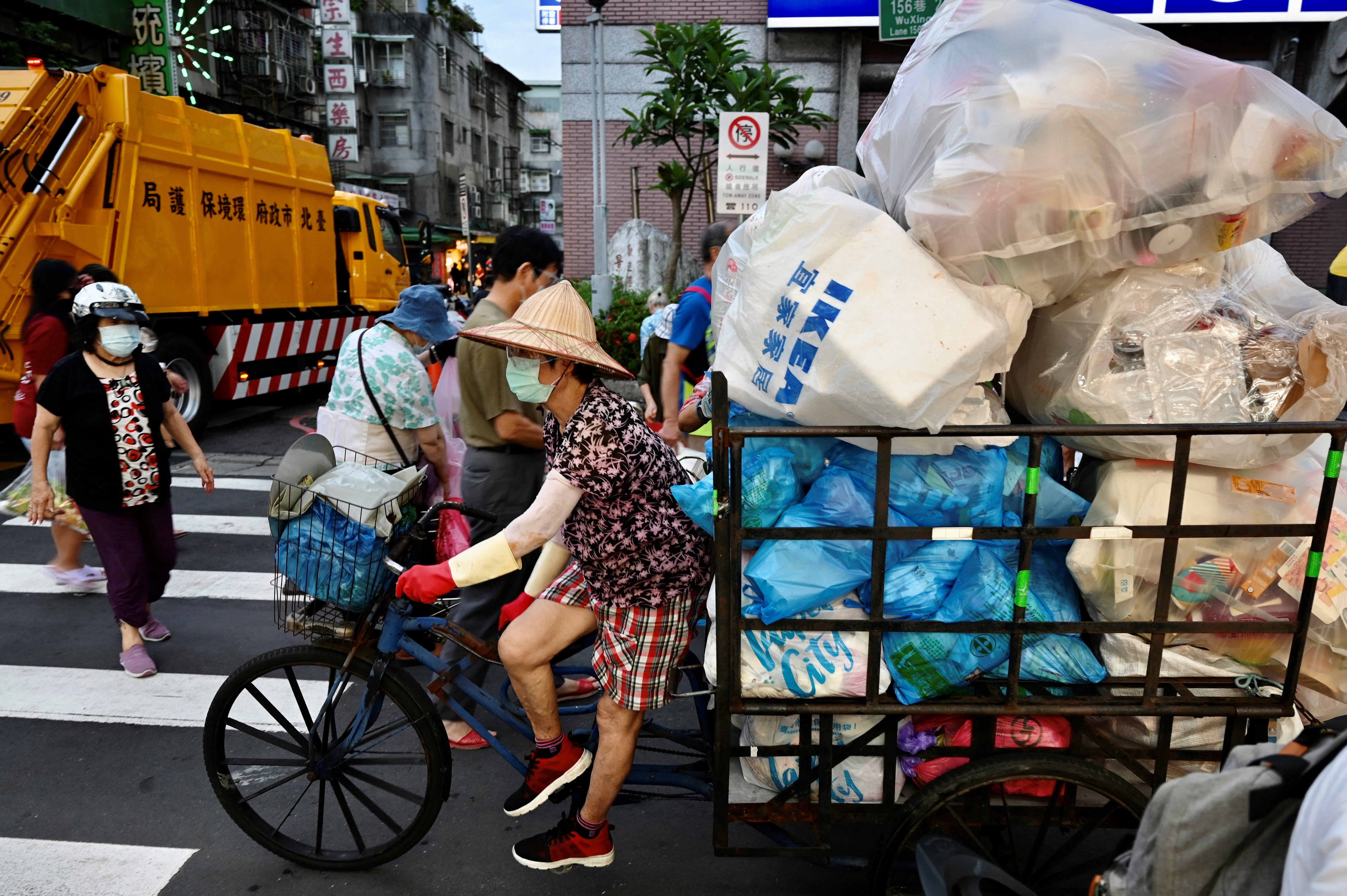 A woman with a tricycle full of rubbish arrives to offload it into a truck