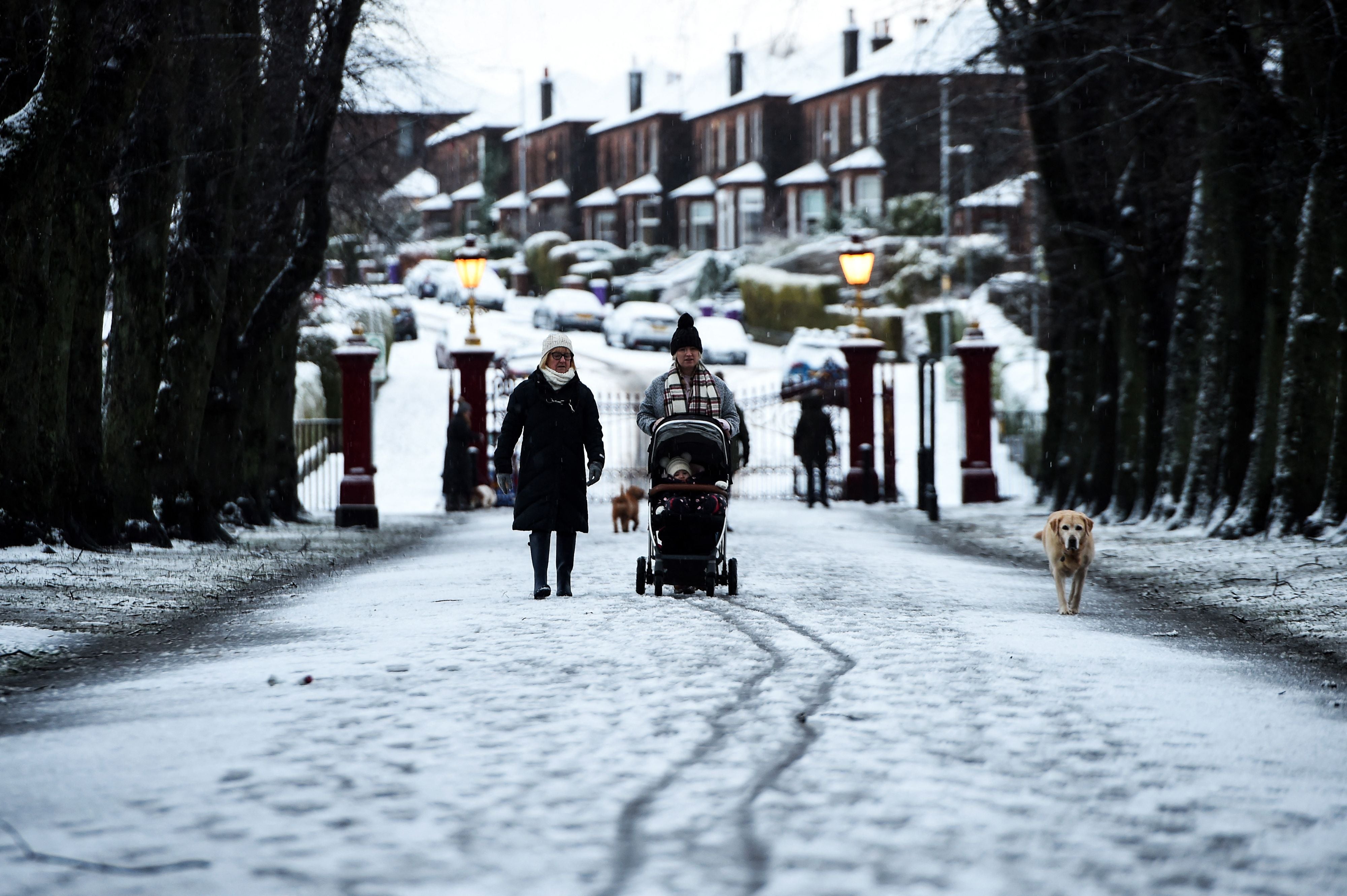 People walk with a dog in the snow in Victoria Park, in the West End of Glasgow