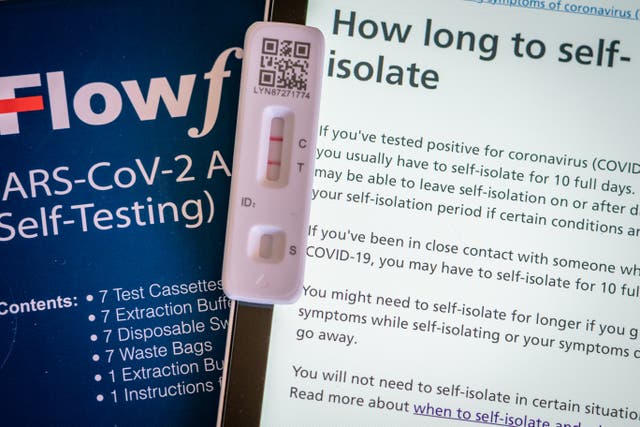A positive lateral flow test cassette placed next to advice from the NHS website (Aaron Chown/PA)