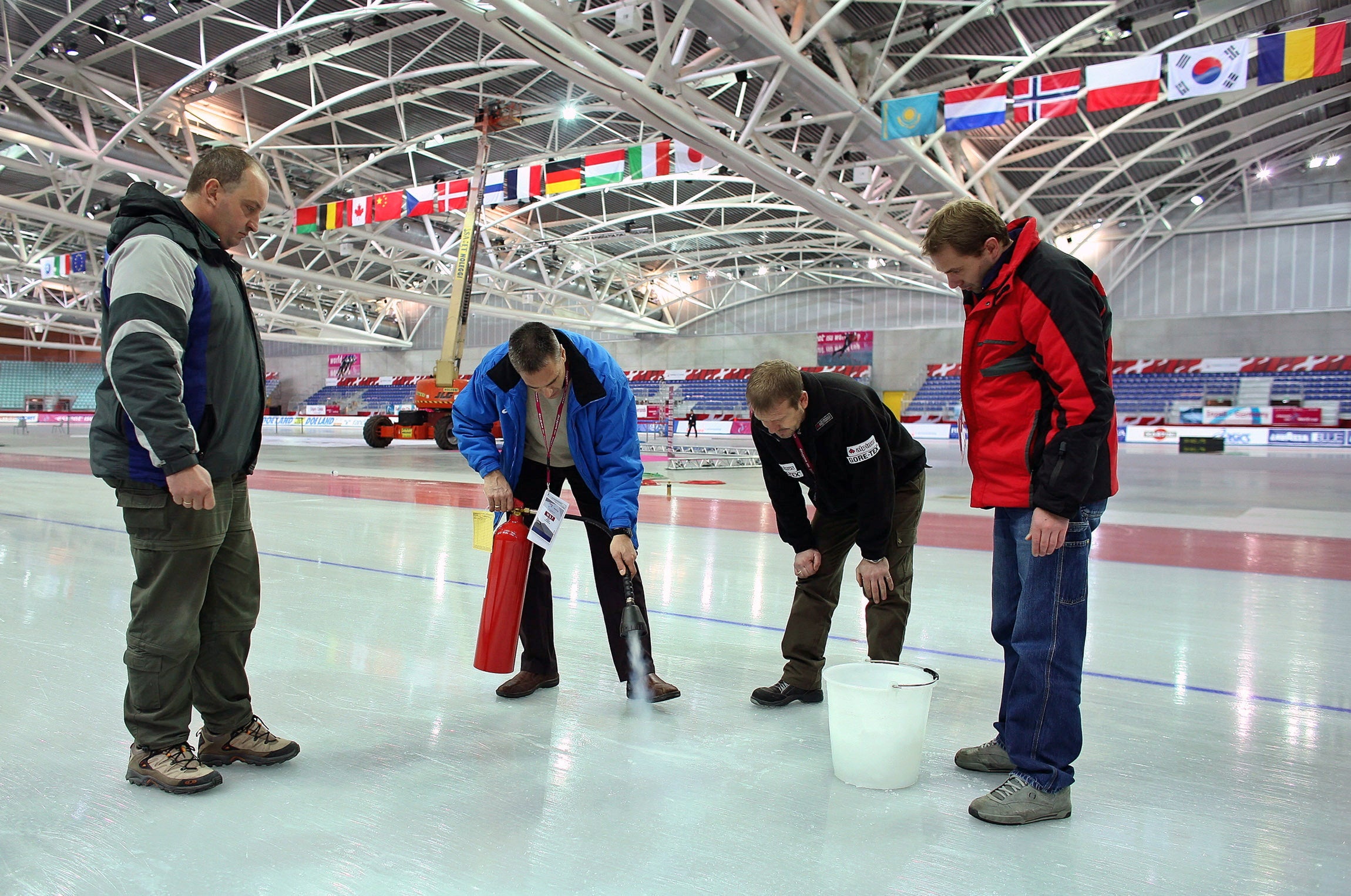 Canadian Ice Master Mark Messer (2nd L) uses a fire extinguisher to repair the ice at the 2006 Olympic speedskating venue "The Oval Lingotto" as his colleagues watch during a team practise for the World Cup Speed Skating tournament in Turin December 8, 2005. REUTERS/Jerry Lampen/File Photo