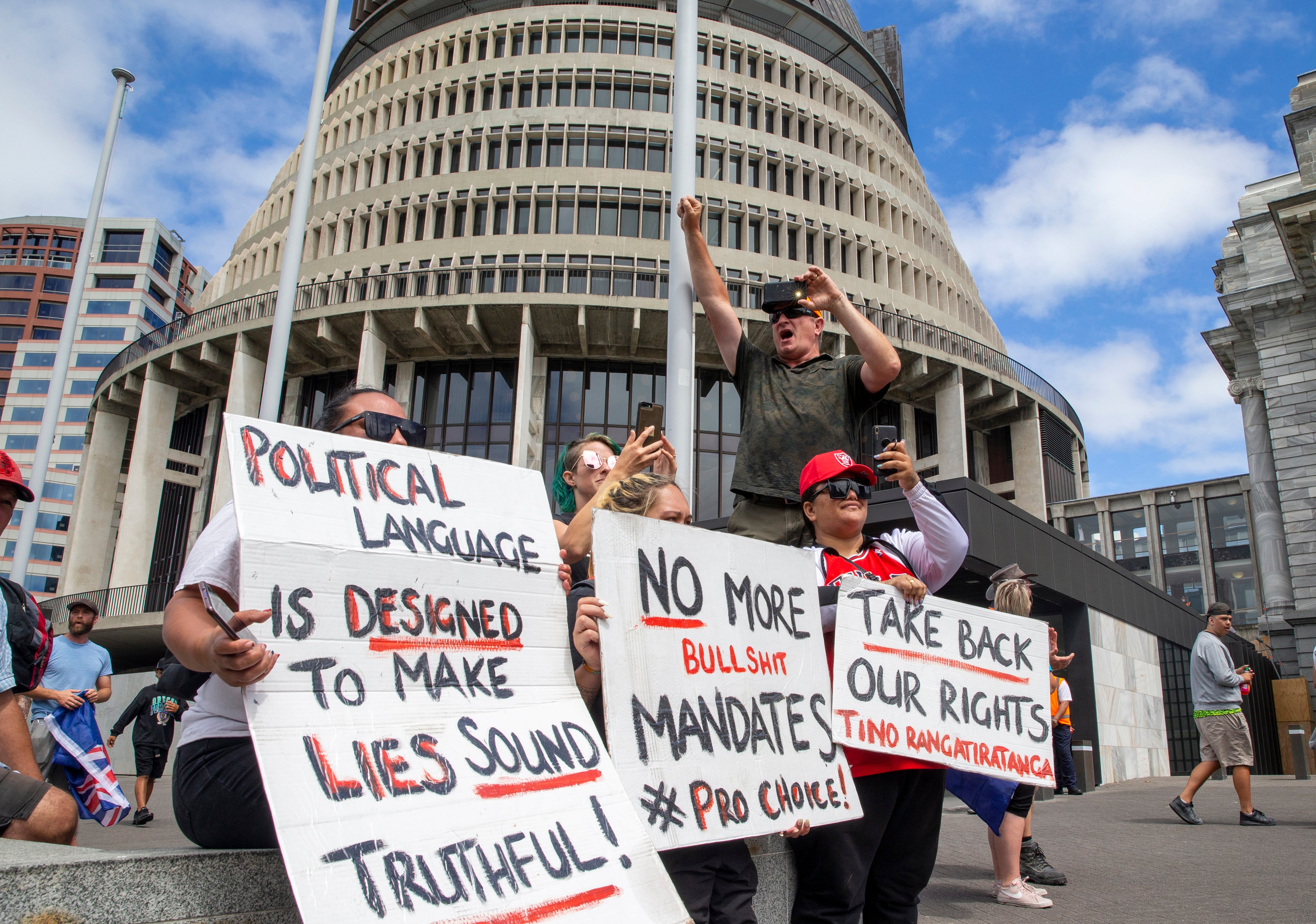 Protesters hold placards as they support the convoy of vehicles blocking New Zealand's Parliament in Wellington