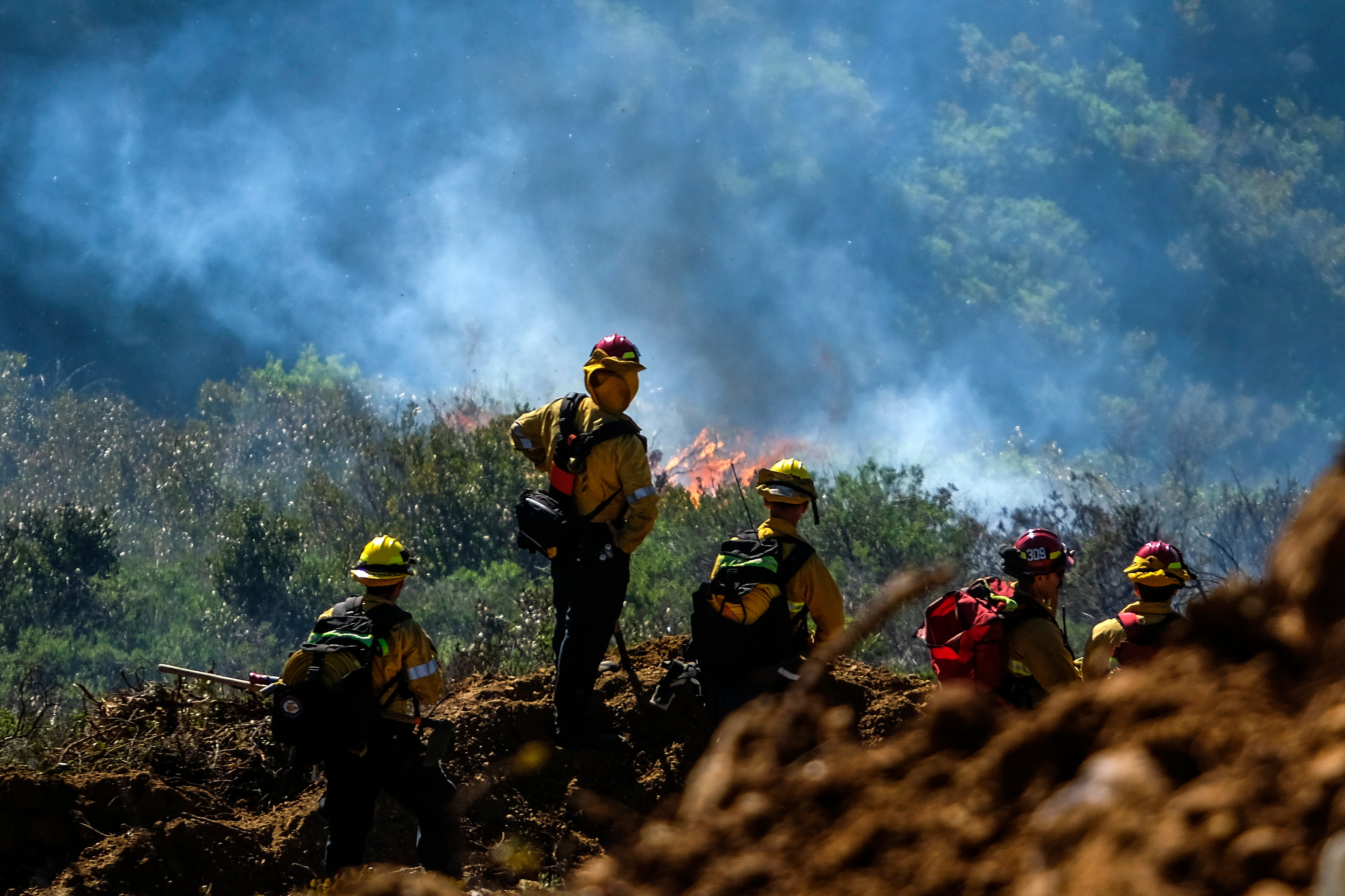 Firefighters watch as flames advance up a hillside