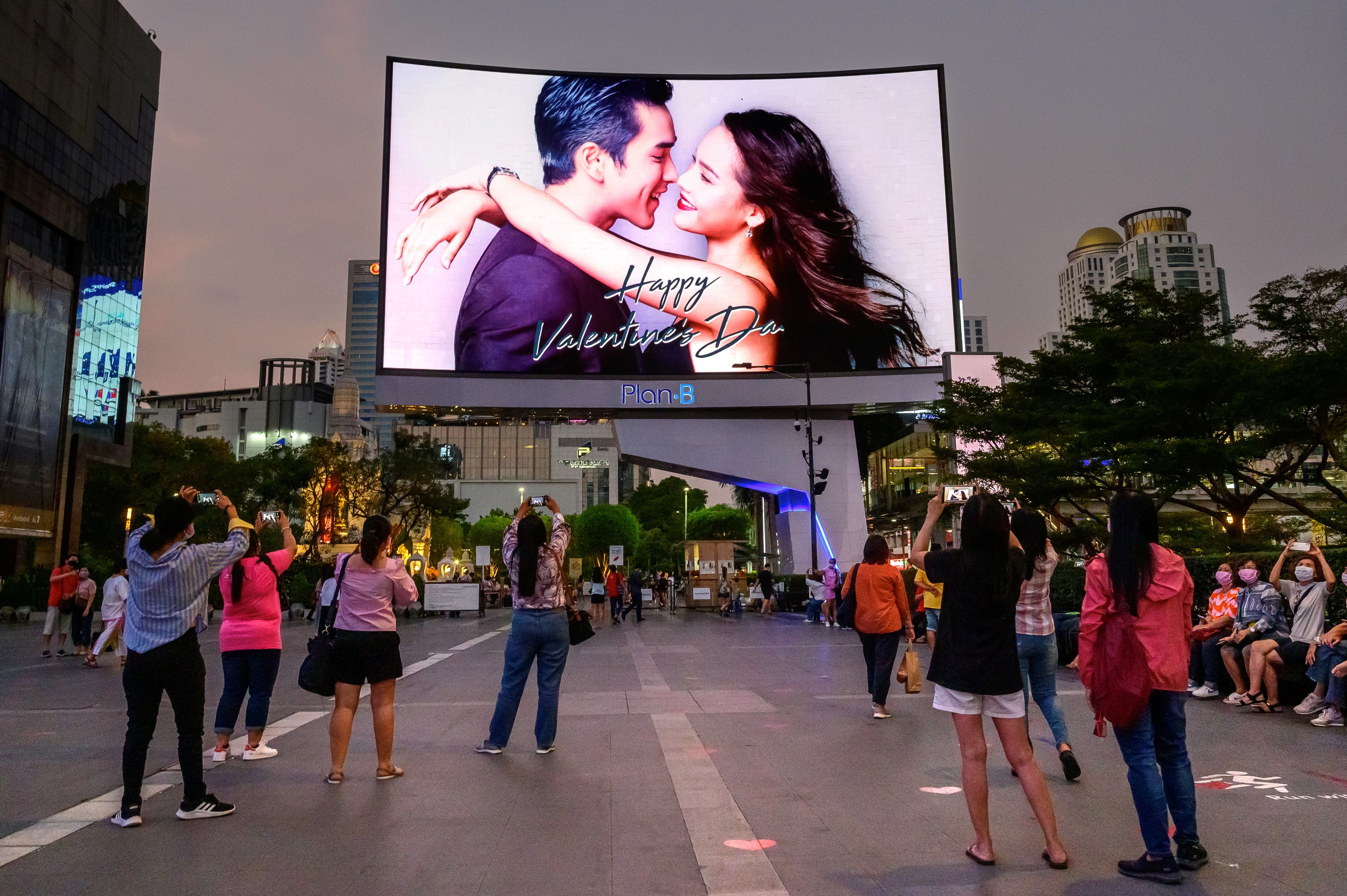People take photographs of a screen wishing a happy Valentine’s day, in Bangkok on 14 February 2021