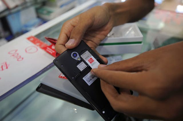 <p>A mobile phone salesman puts an Ooredoo SIM card into a new handset for a customer at a mobile phone shop in Yangon on August 2, 2014.</p>