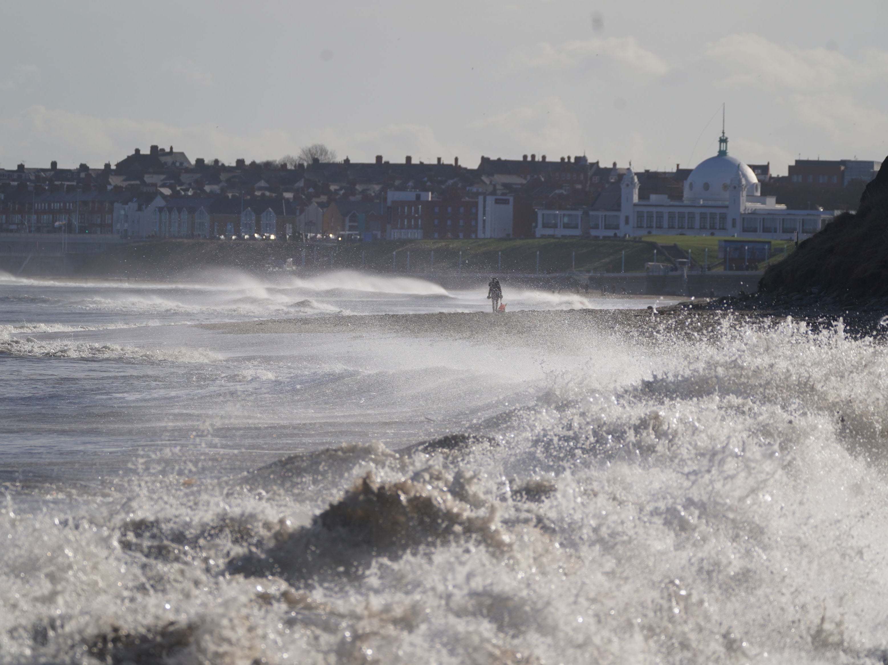 A dog walker on Whitley bay beach as big waves hit the shoreline on 15 February 2022