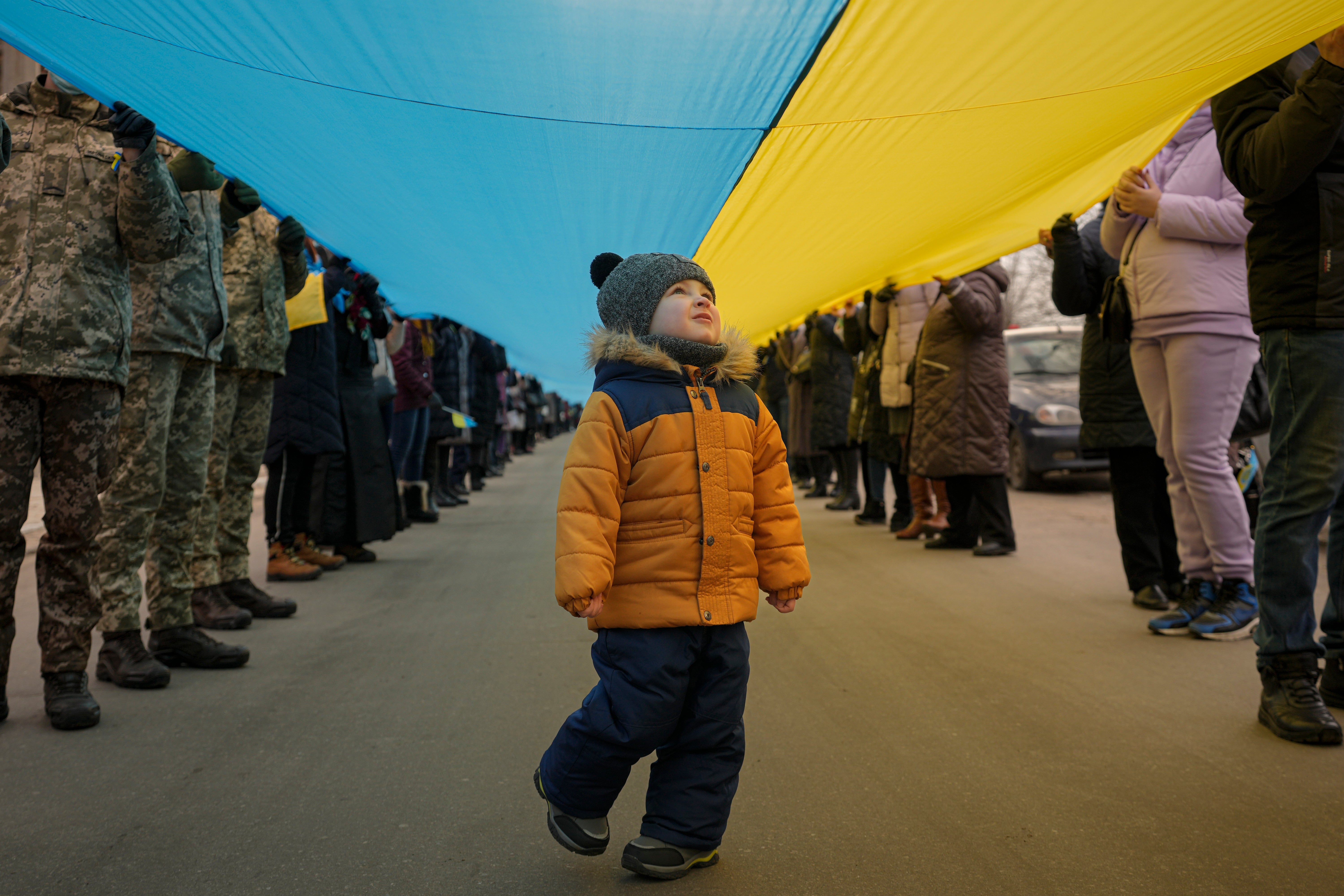 A child walks under a large Ukrainian flag carried by people marking a "day of unity" in Sievierodonetsk, the Luhansk region, eastern Ukraine, Wednesday, Feb. 16, 2022