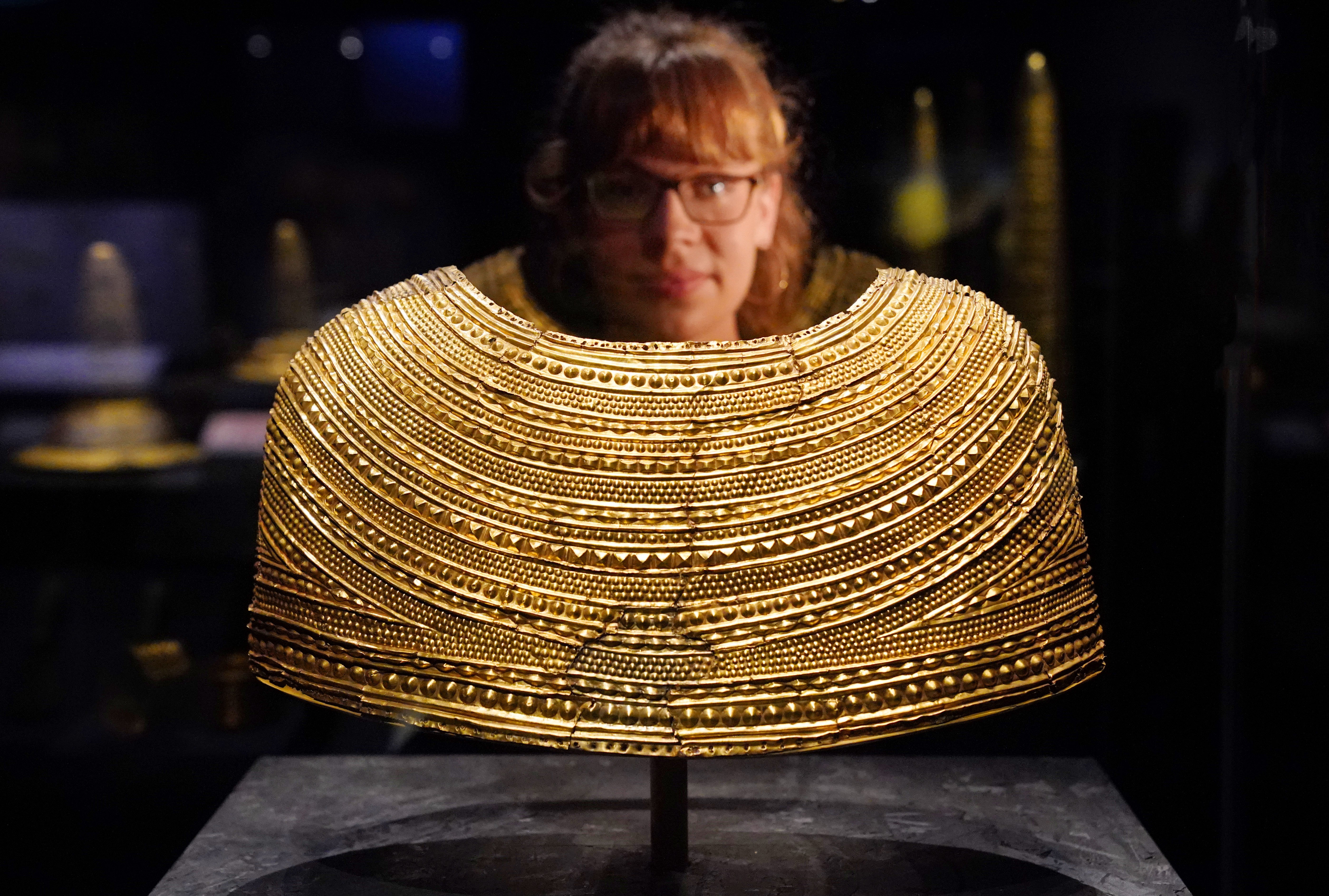 A member of staff observes a gold cape dating from 1600-1900 BC from Mold, Flintshire, Wales (Jonathan Brady/PA)