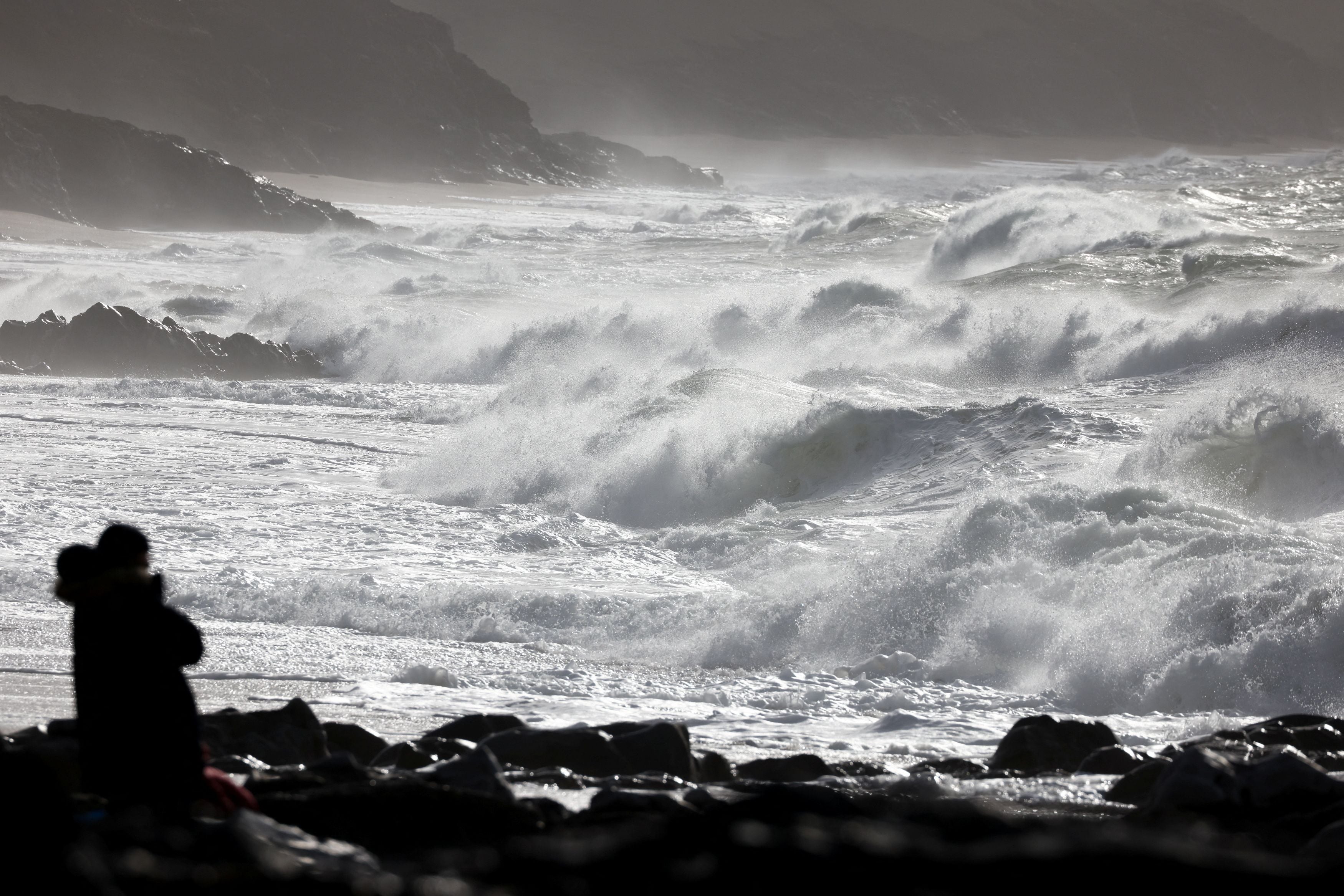 A person watches as waves break on Porthleven beach in the wake of Storm Dudley in Porthleven, Cornwall