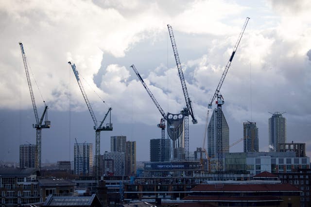 <p>Cranes are seen silhouetted against a cloudy sky in south London</p>