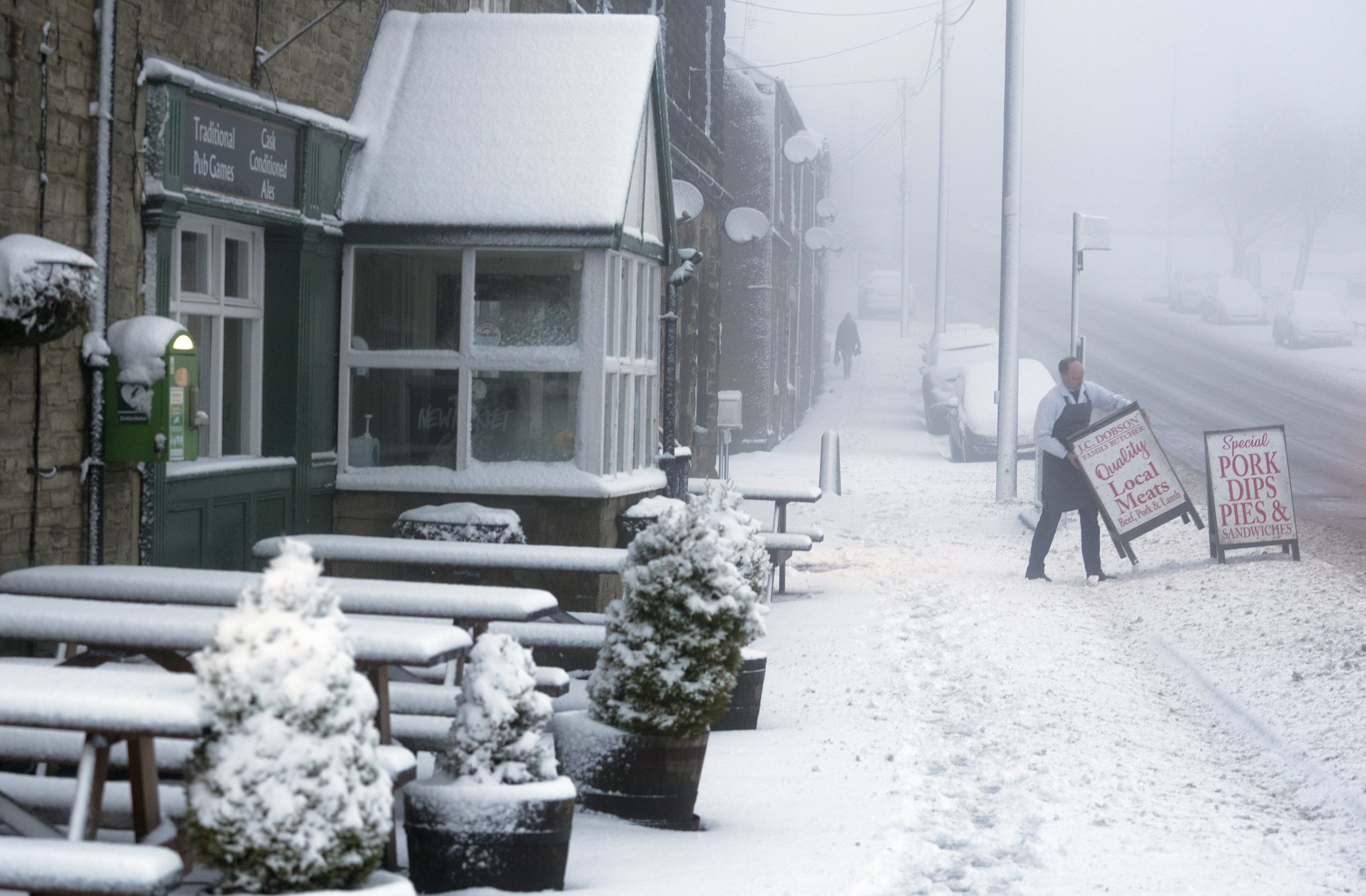 A local butcher carries his shop sign across a snowy pavement in County Durham