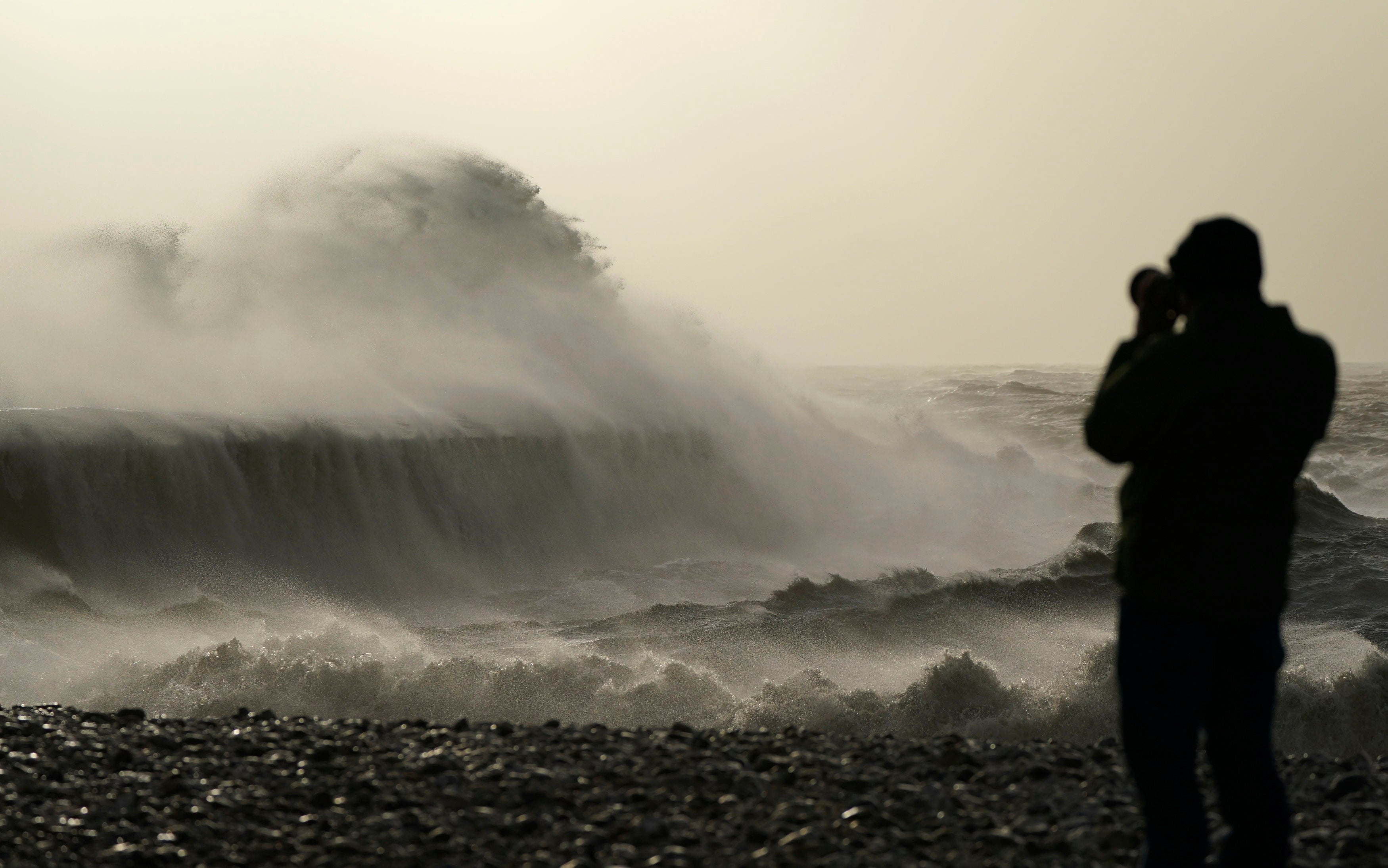 A weatherwatcher take photographs of waves as they crash against the Cobb in Lyme Regis