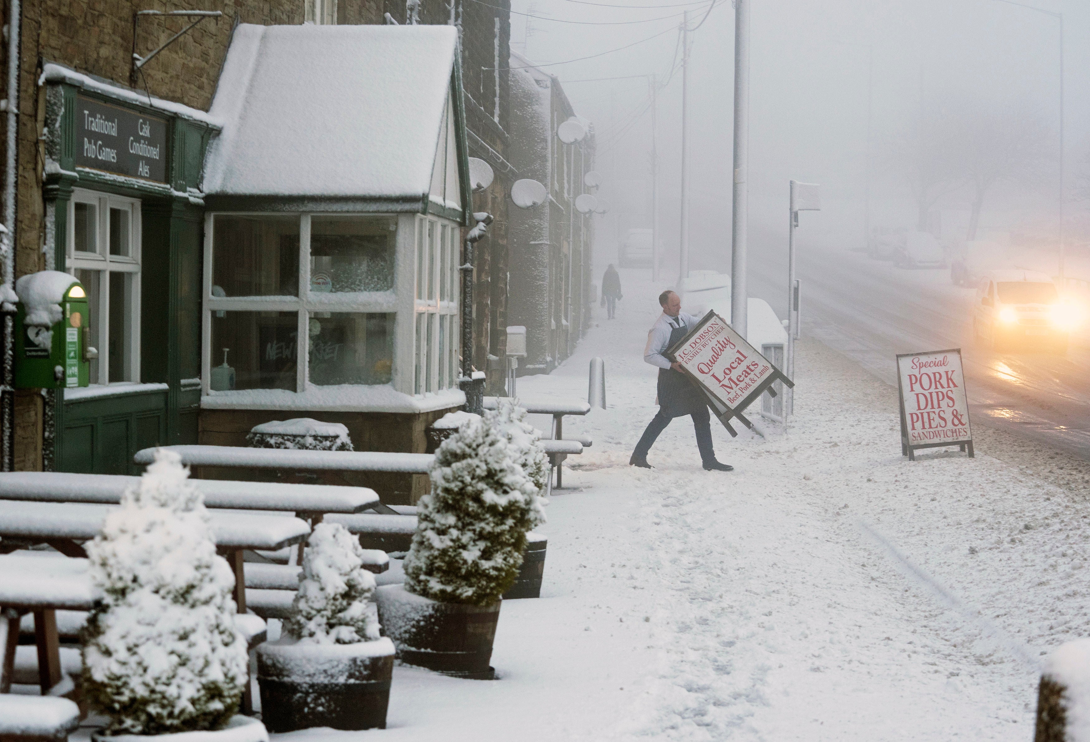 A butcher carries his shop sign across a snowy pavement in Tow Law, County Durham