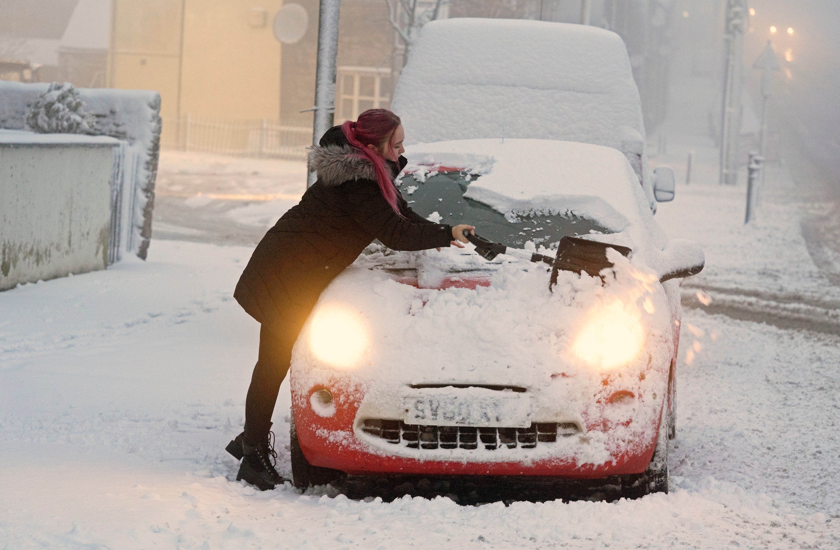 A woman clears snow from her car as Storm Eunice sweeps across the UK