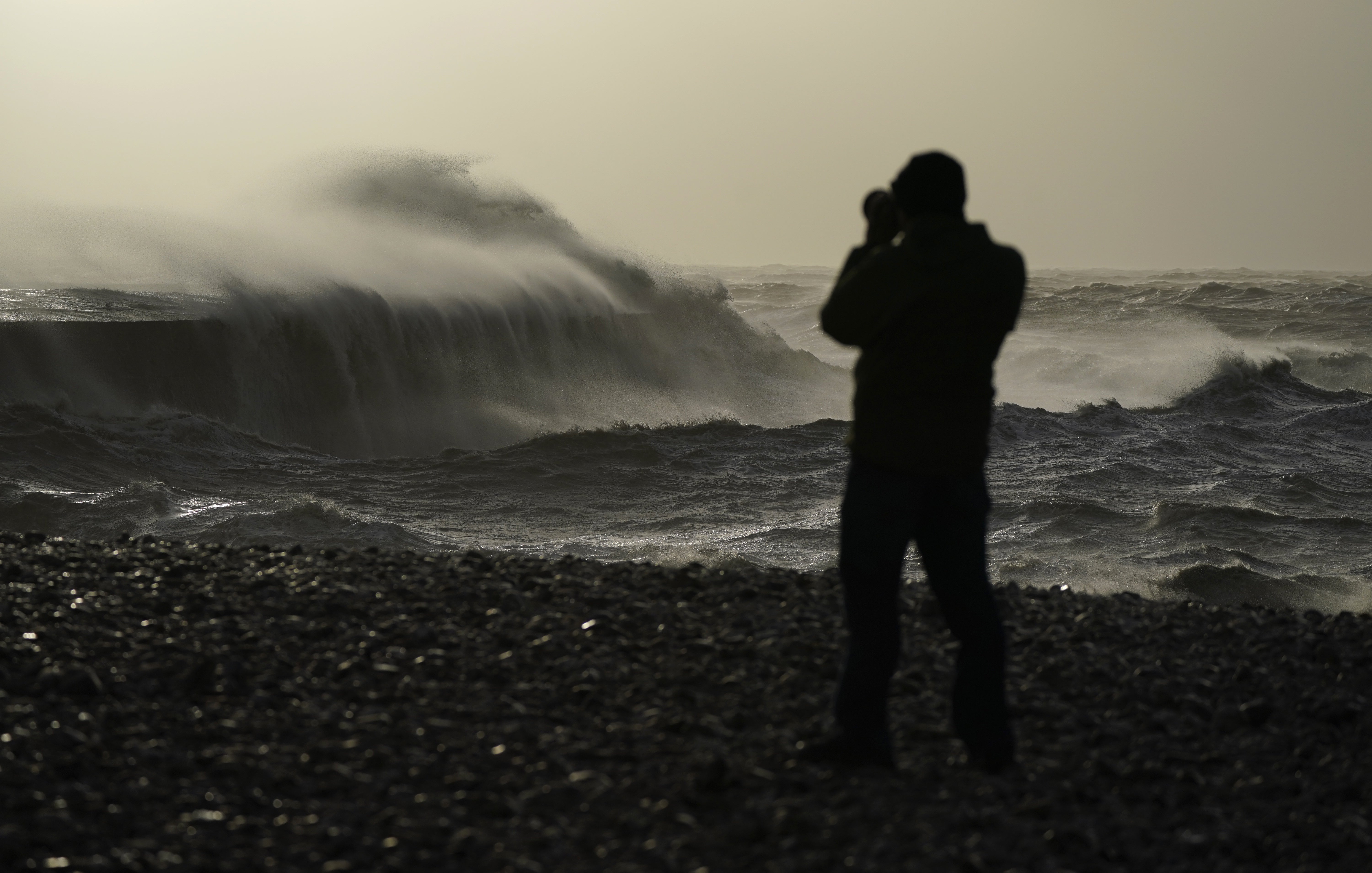 A person take photographs of waves as they crash against the Cobb in Lyme Regis, west Dorset (Andrew Matthews/PA)