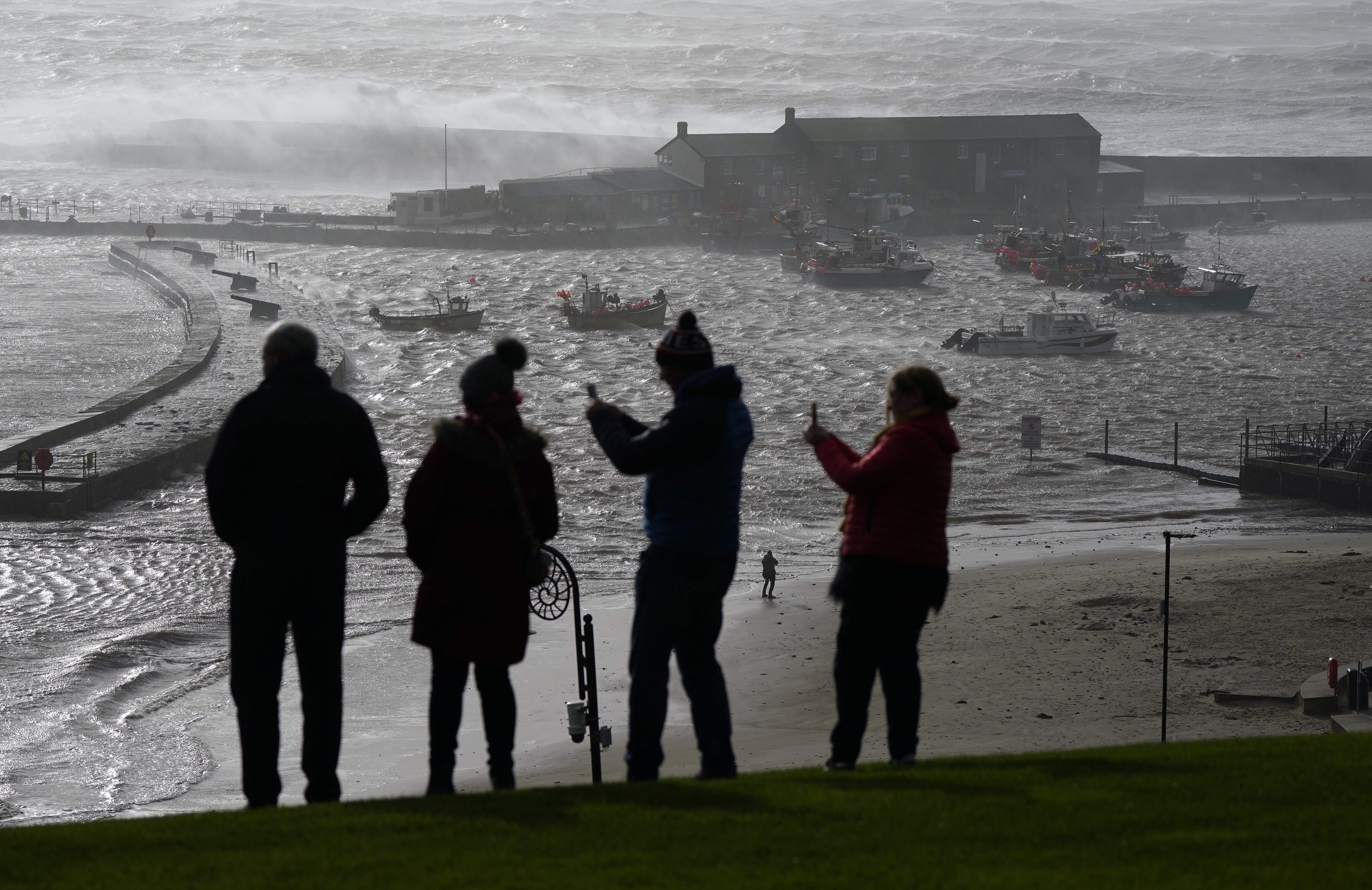 People look out towards the sea as waves crash against the Cobb in Lyme Regis, west Dorset (Andrew Matthews/PA)