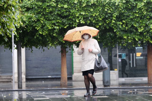 A woman wearing a protective face mask shelters from the rain on Dublin’s O’Connell Street (Brian Lawless/PA)