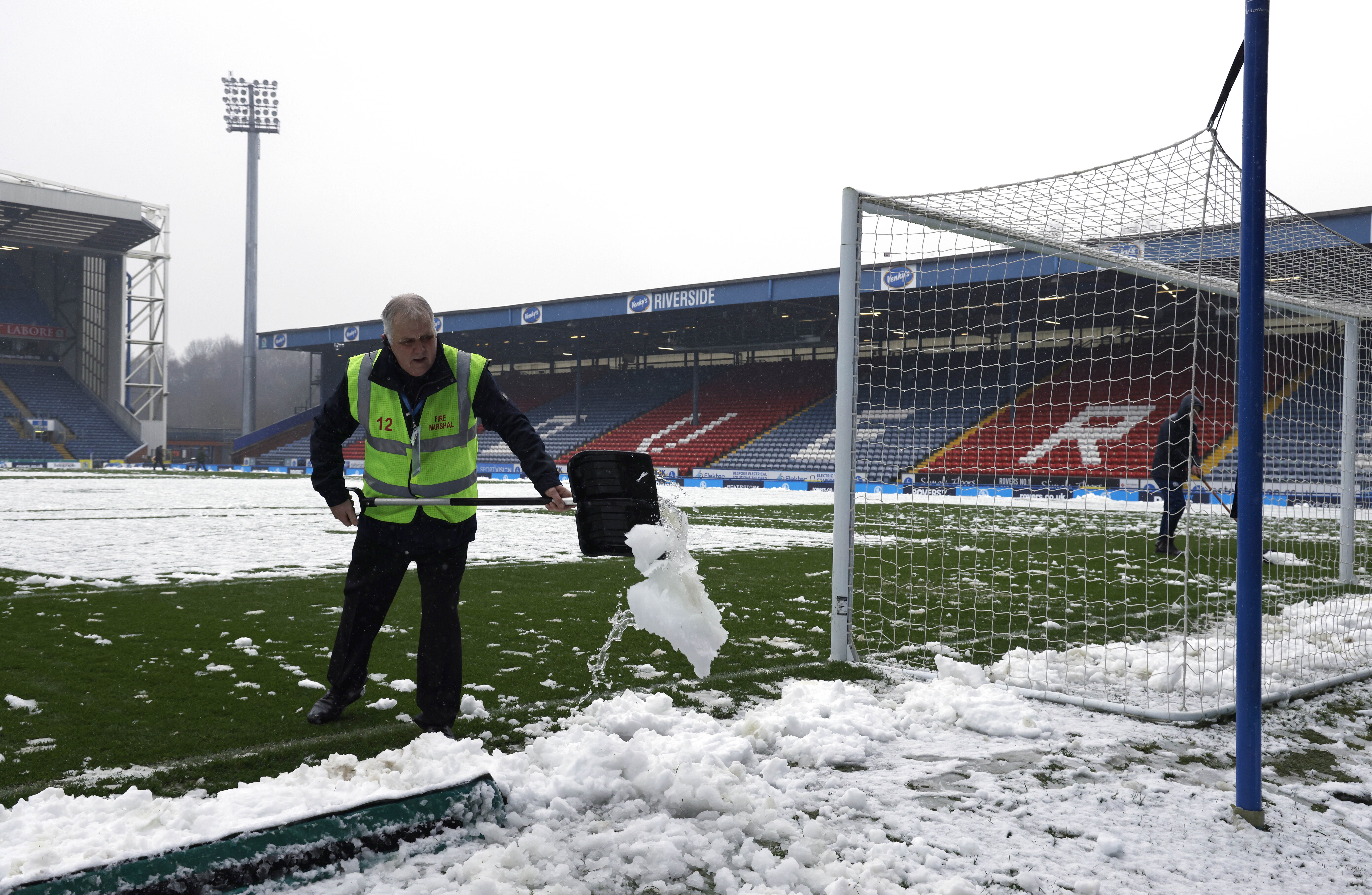 Staff clearing snow from the pitch before the Rovers game was cancelled
