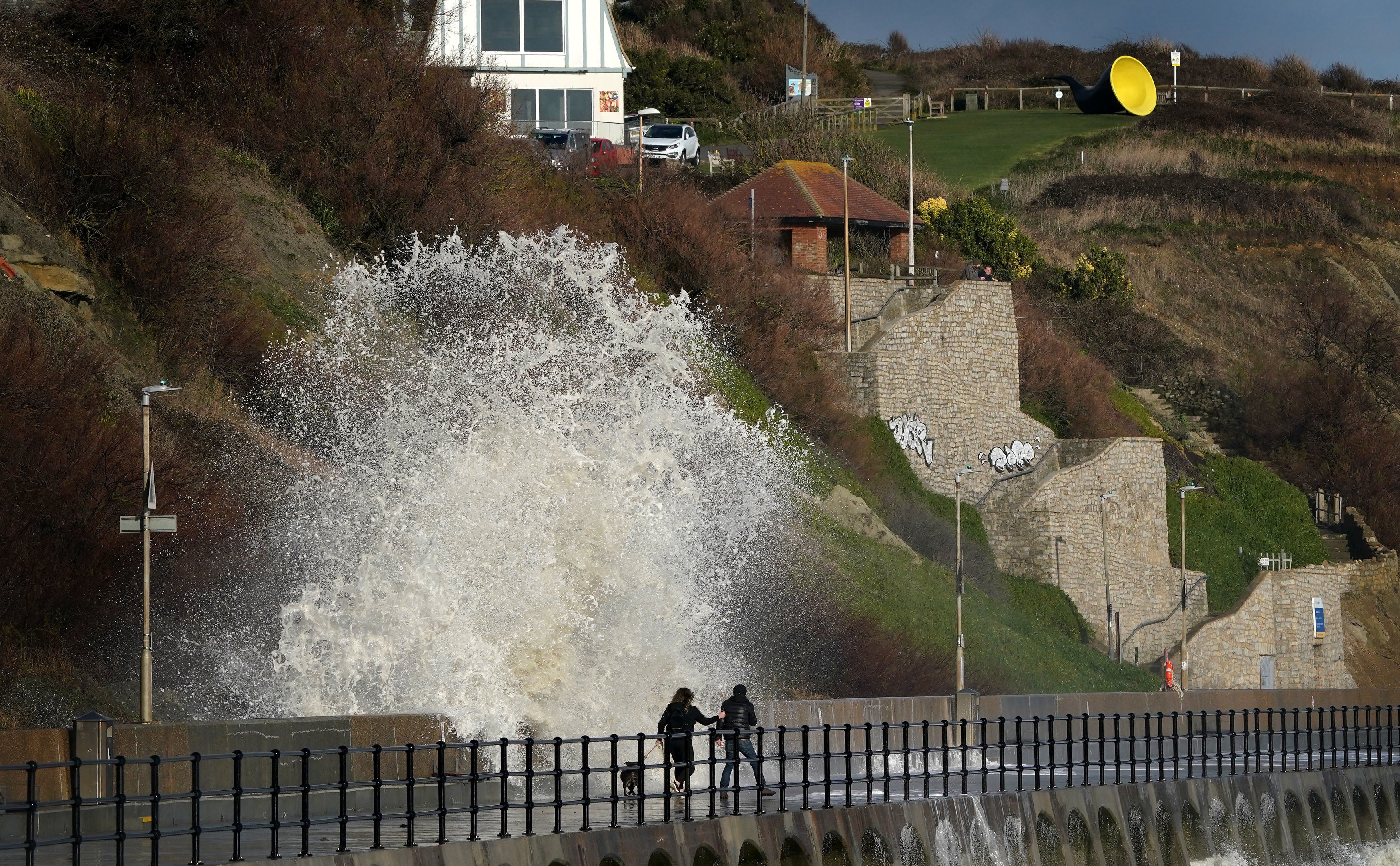 A couple are hit by a wave during strong winds on the promenade in Folkestone, Kent