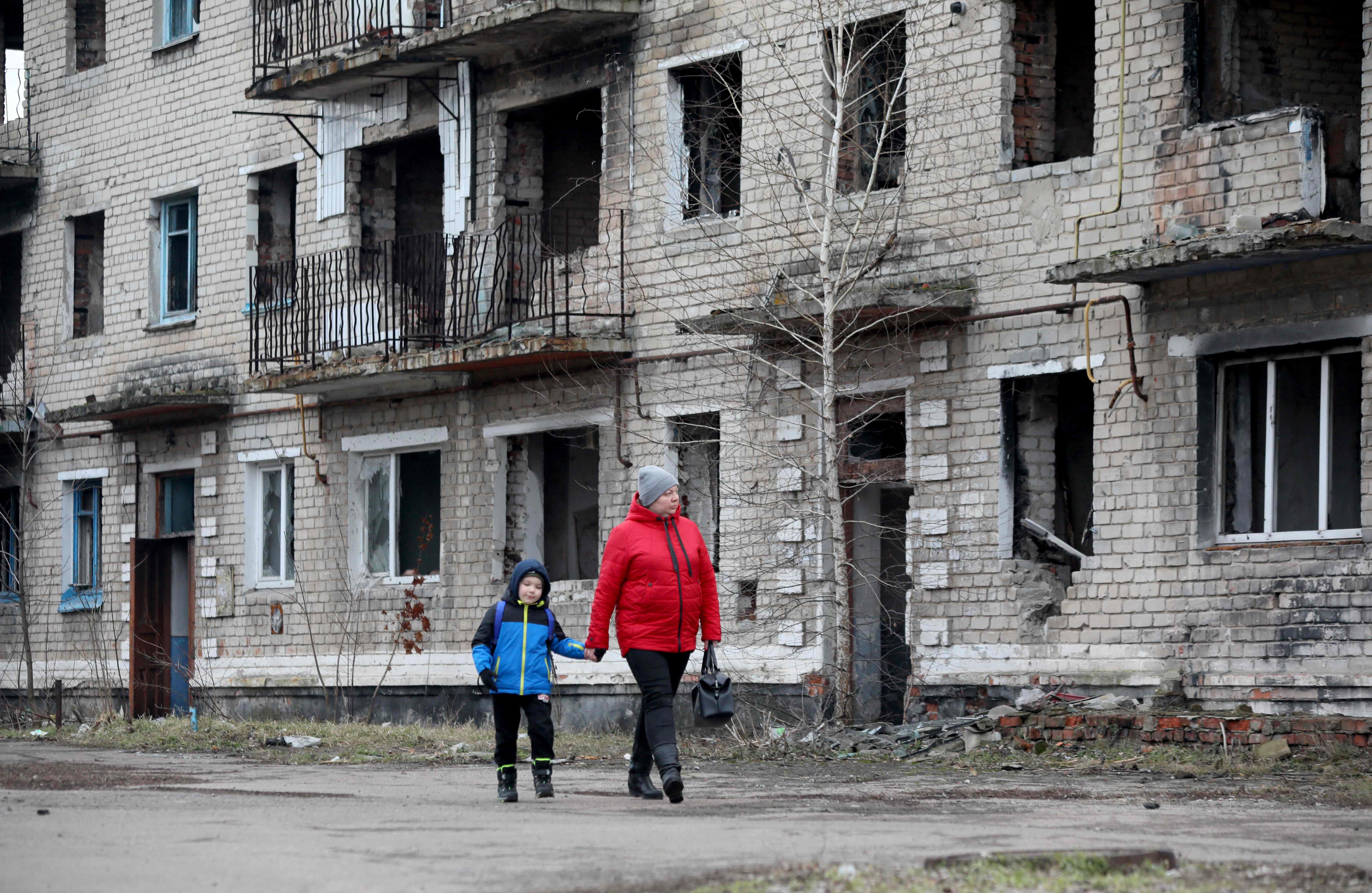 A woman with a boy walk past an old destroyed building in the small town of Krasnogorivka, Donetsk