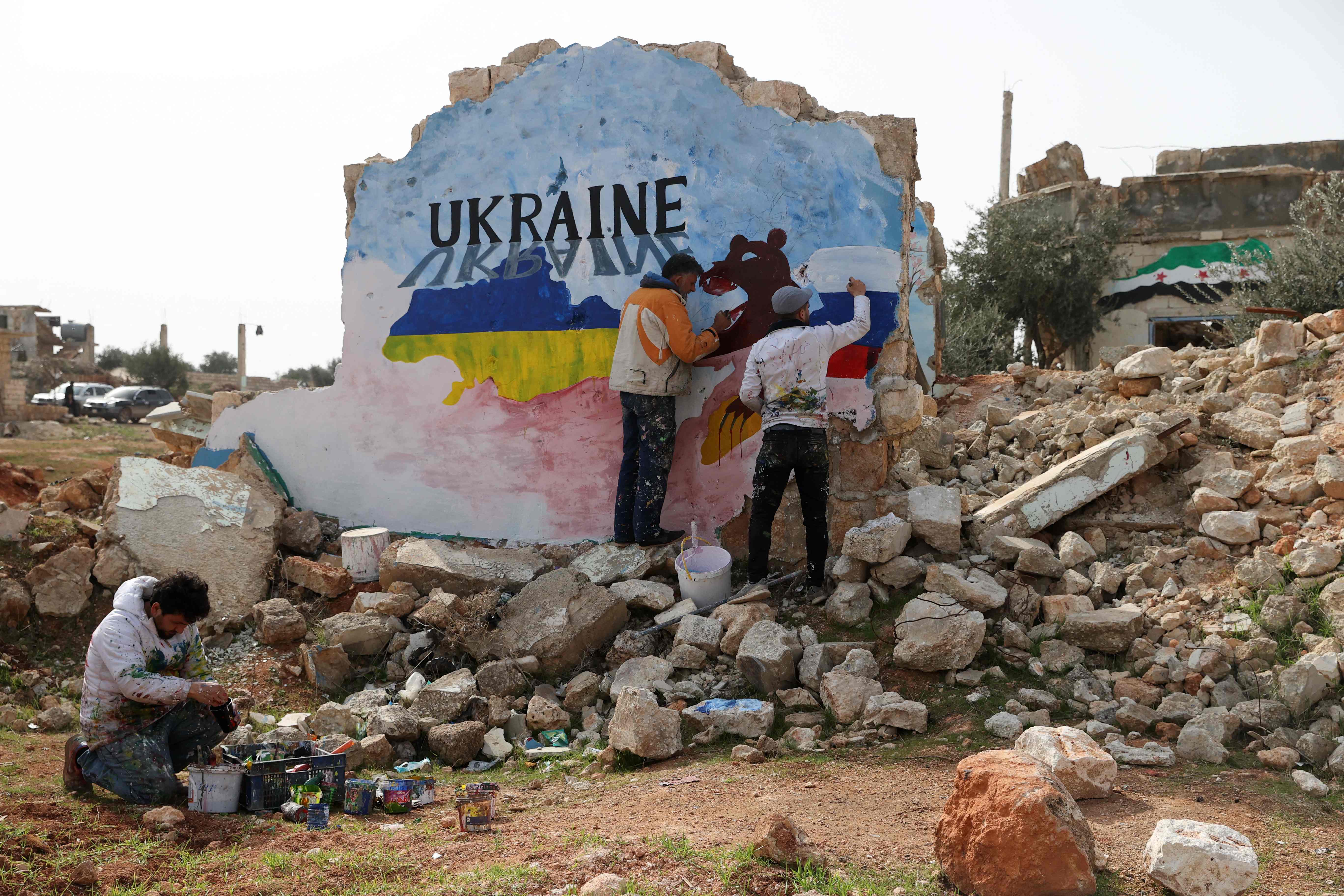 Syrian artists Aziz Asmar and Anis Hamdoun paint a mural amid the destruction, depicting the colours of the Russian and Ukranian flags, to protest against Russia's military operation in Ukraine, in the rebel-held town of Binnish in Syria's northwestern Idlib province