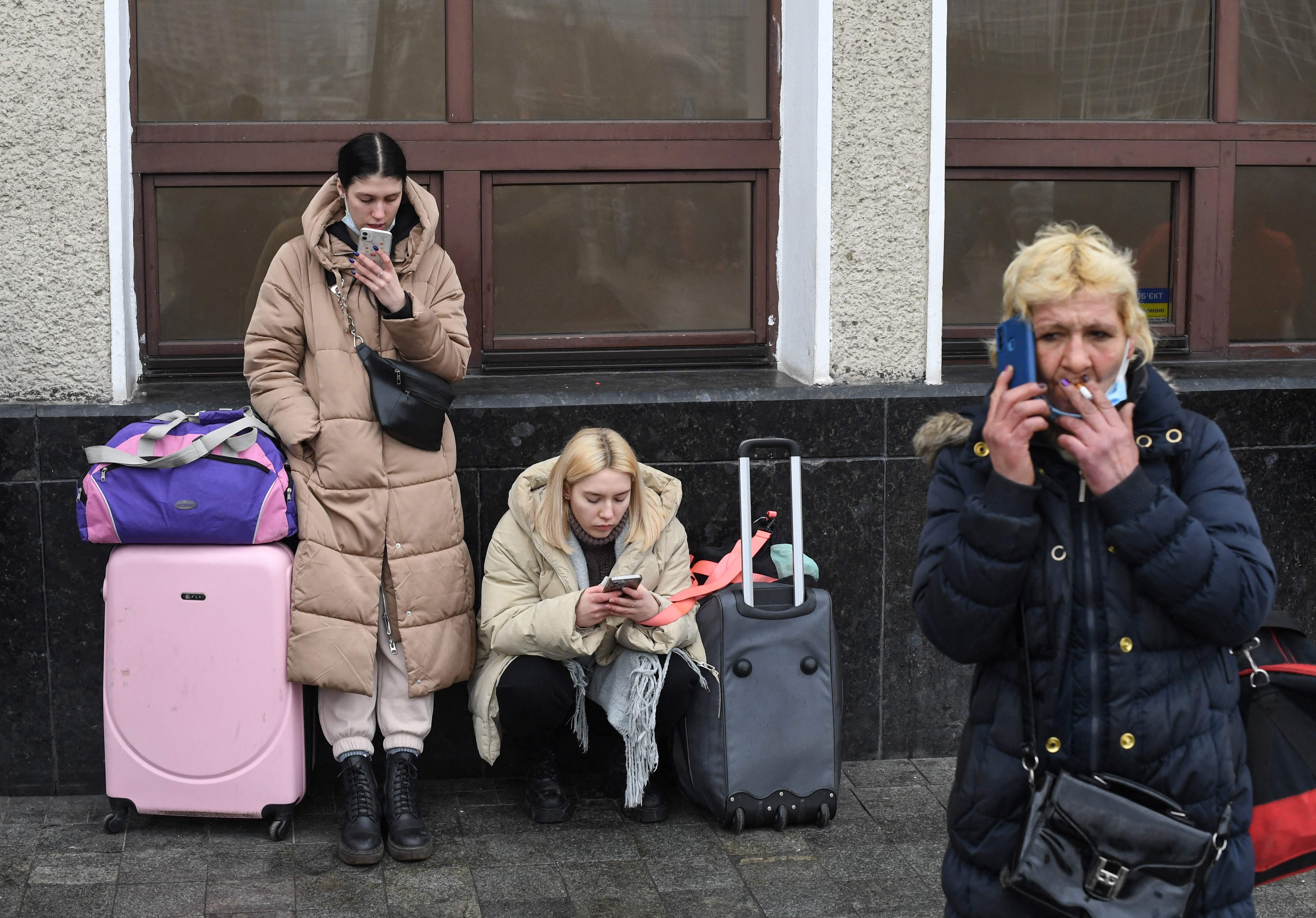 Women use their phones as they wait with bags and suitcases near Kiev-Pasazhyrskyi railway station