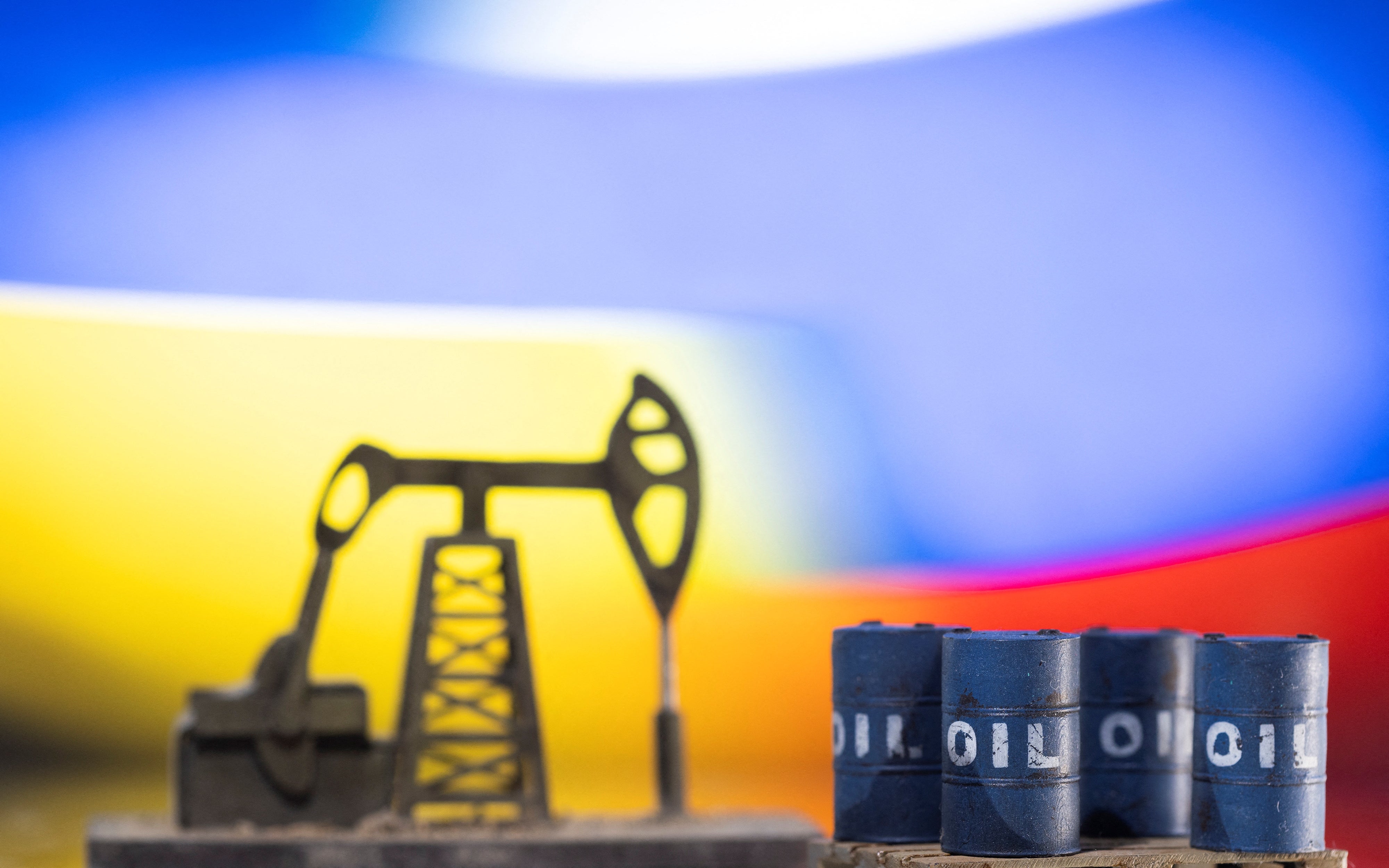 <p>Illustration: Models of oil barrels and a pump jack are displayed in front of Ukrainian and Russian flag colors</p>