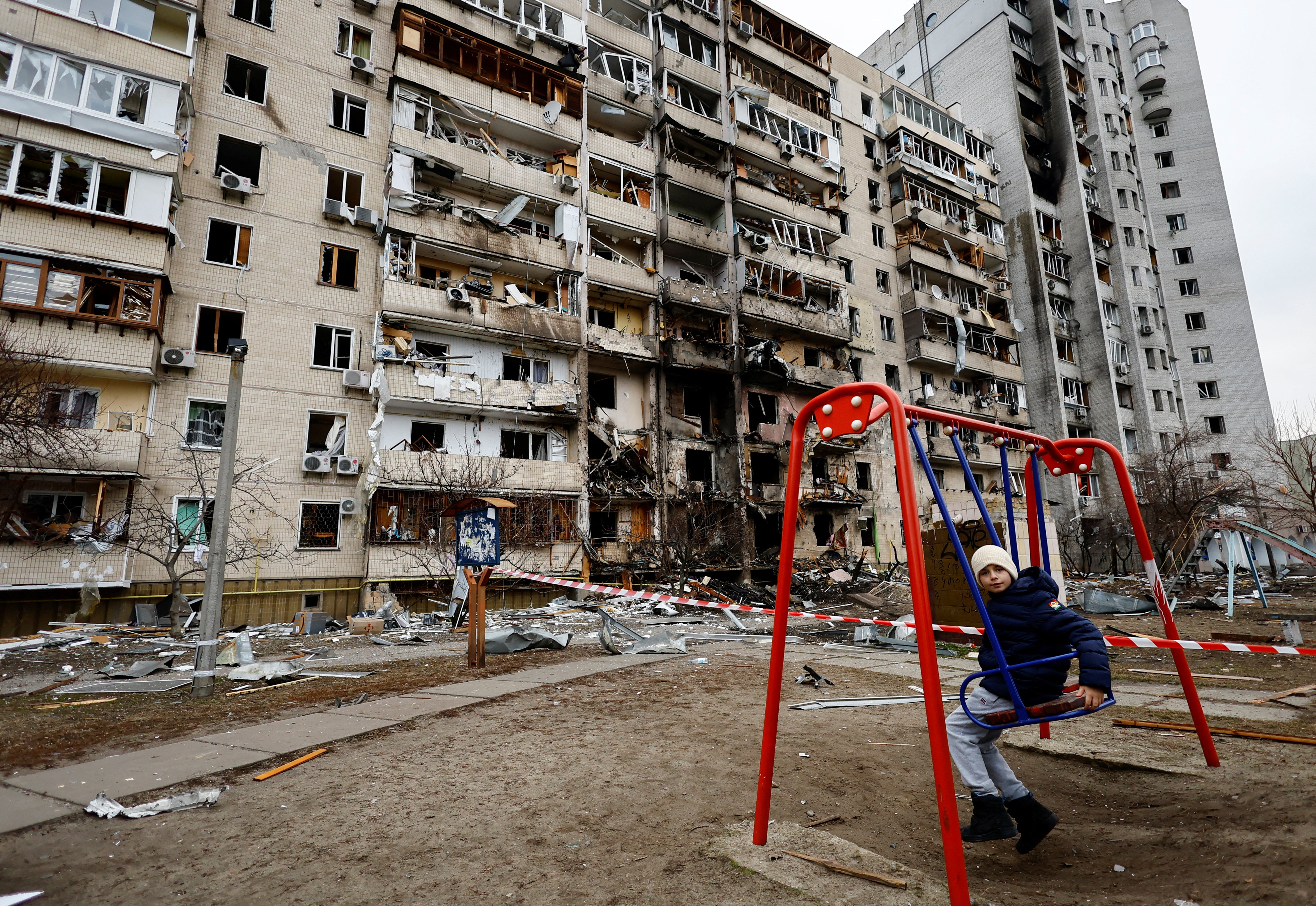 A child sits on a swing in front of a damaged residential building in Kyiv