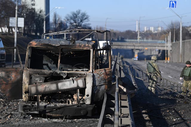 <p>Ukrainian soldiers stand by a burnt army vehicle on the west side of Kyiv</p>