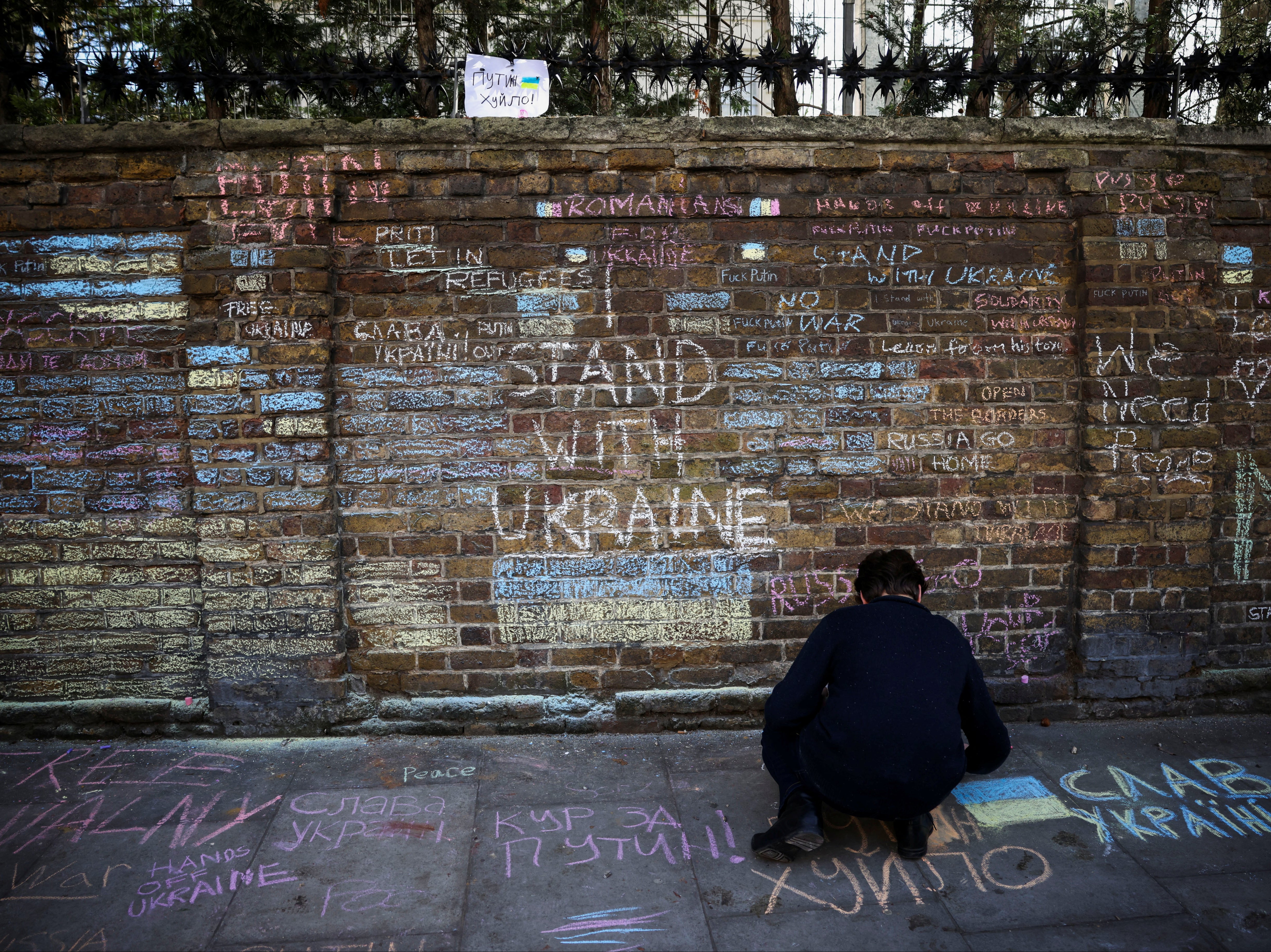 A protester writes on a pavement in front of signs on the wall of the Russian embassy in London during a protest against the war against Ukraine