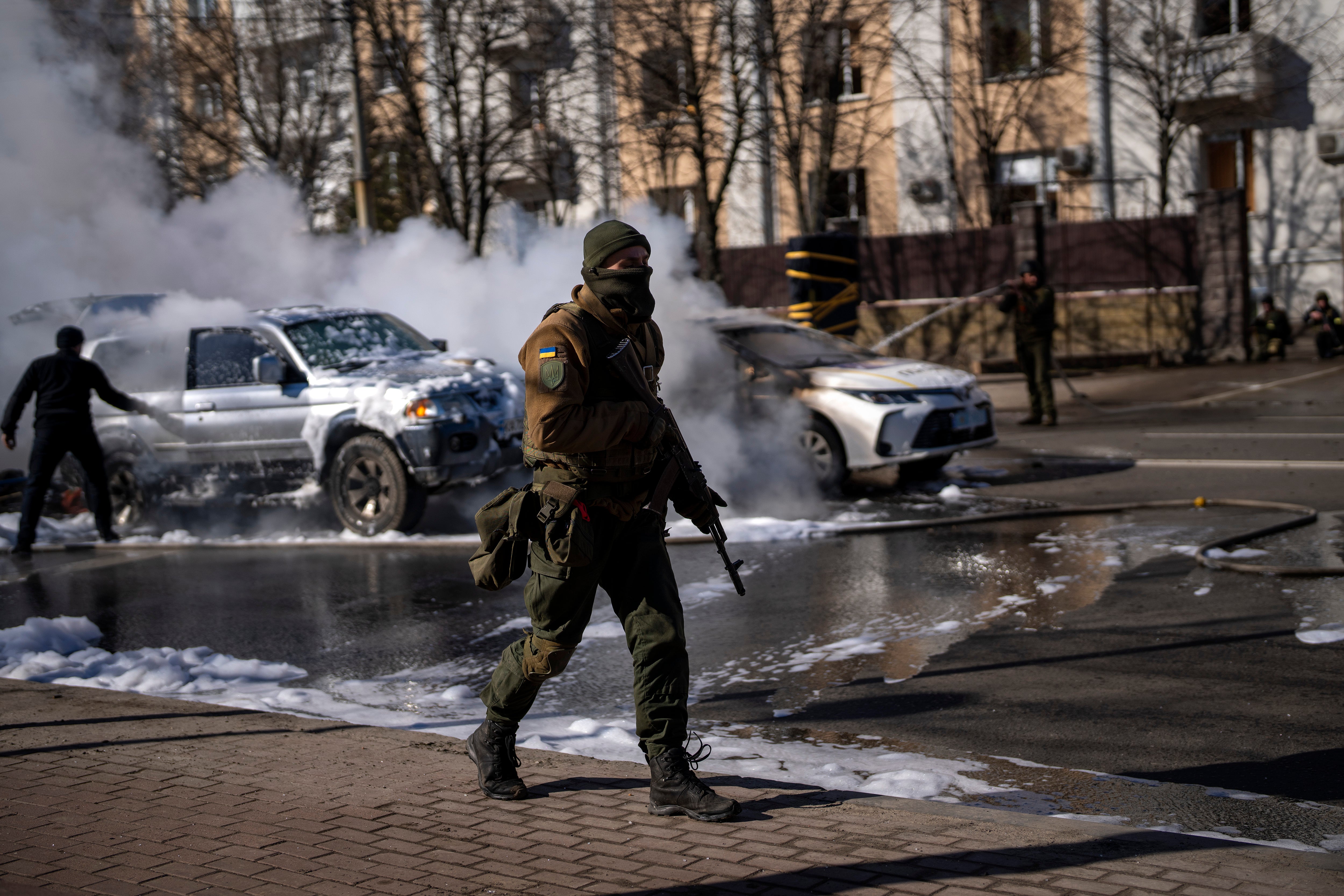 Ukrainian soldiers take positions outside a military facility as two cars burn in a Kyiv street, on Saturday