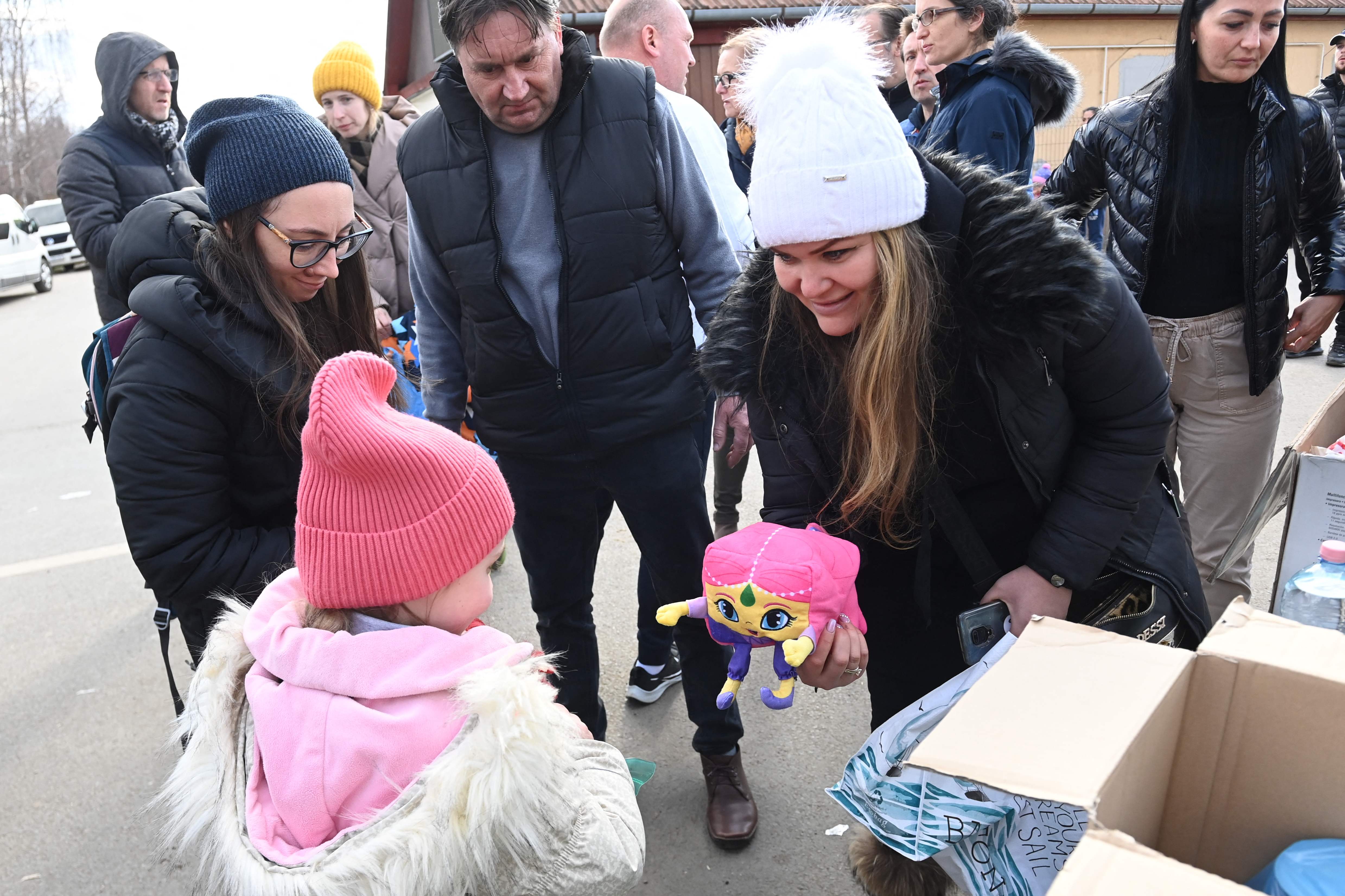 A woman offers a toy to a girl after Ukrainian refugees crossed the Ukrainian-Hungarian border