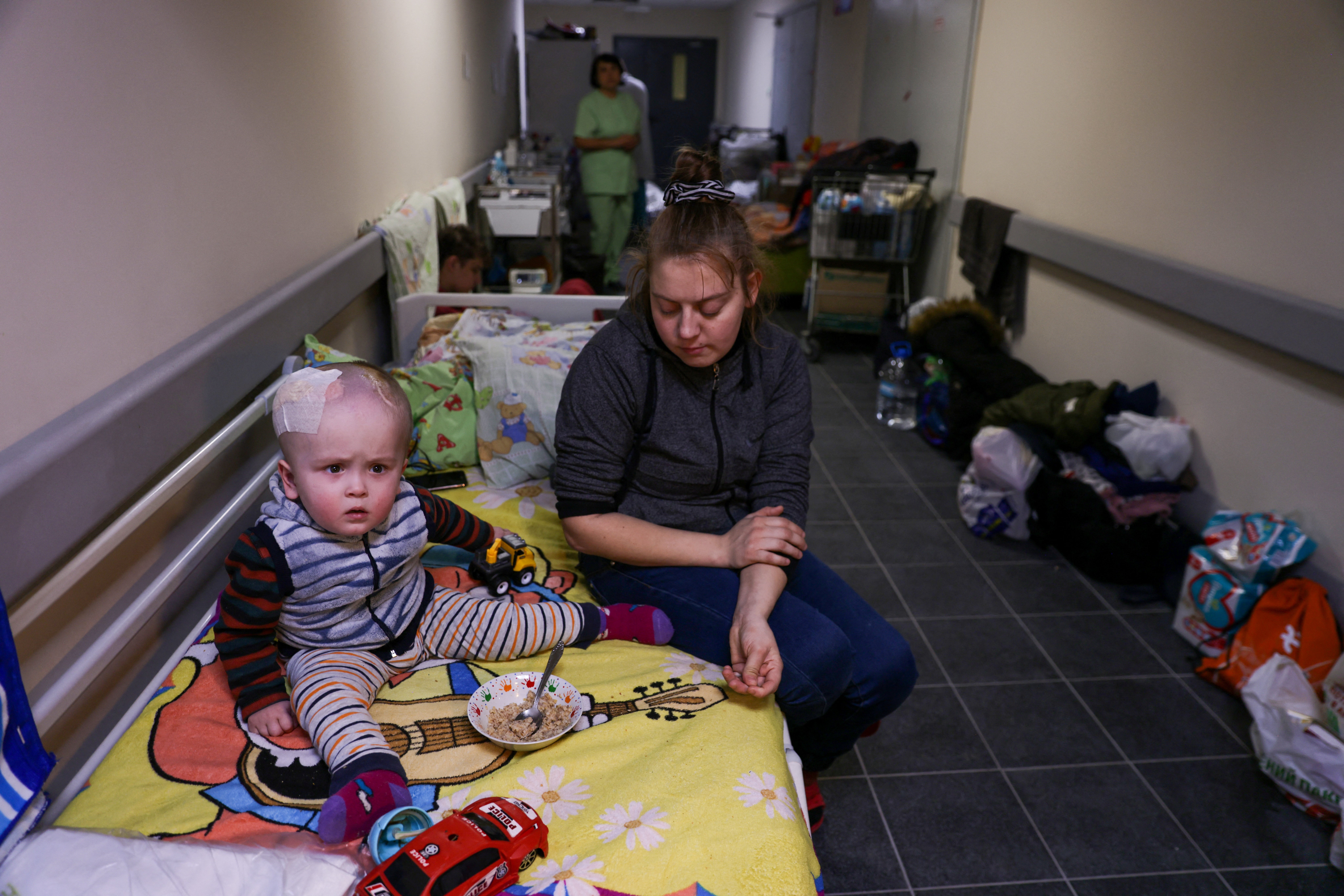 A woman sits next to a child patient whose treatments is underway, in the hallways of basement floors of Okhmadet Children's Hospital, as Russia's invasion of Ukraine continues