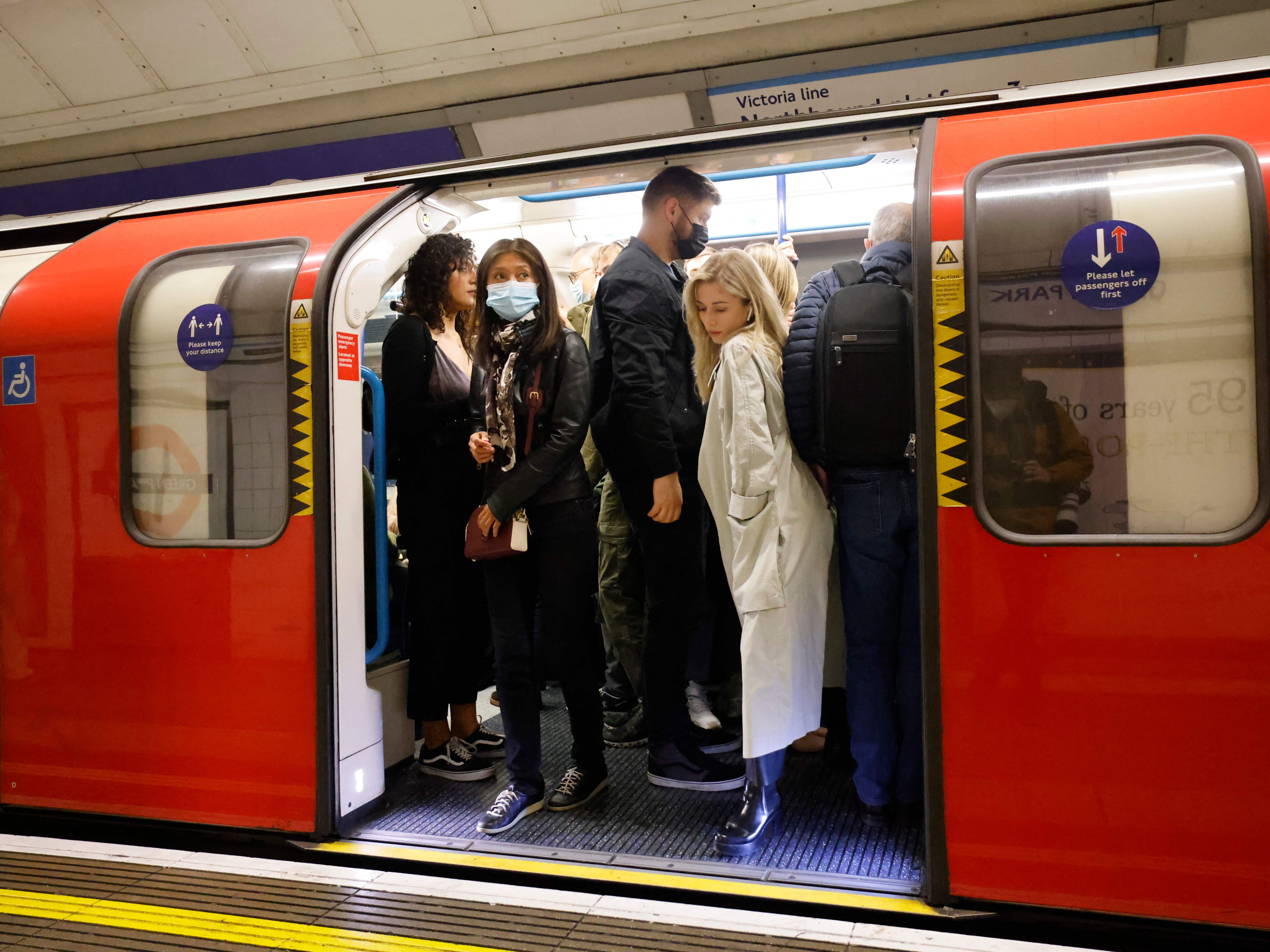 People, some wearing face masks, travel in a packed London Underground tube train