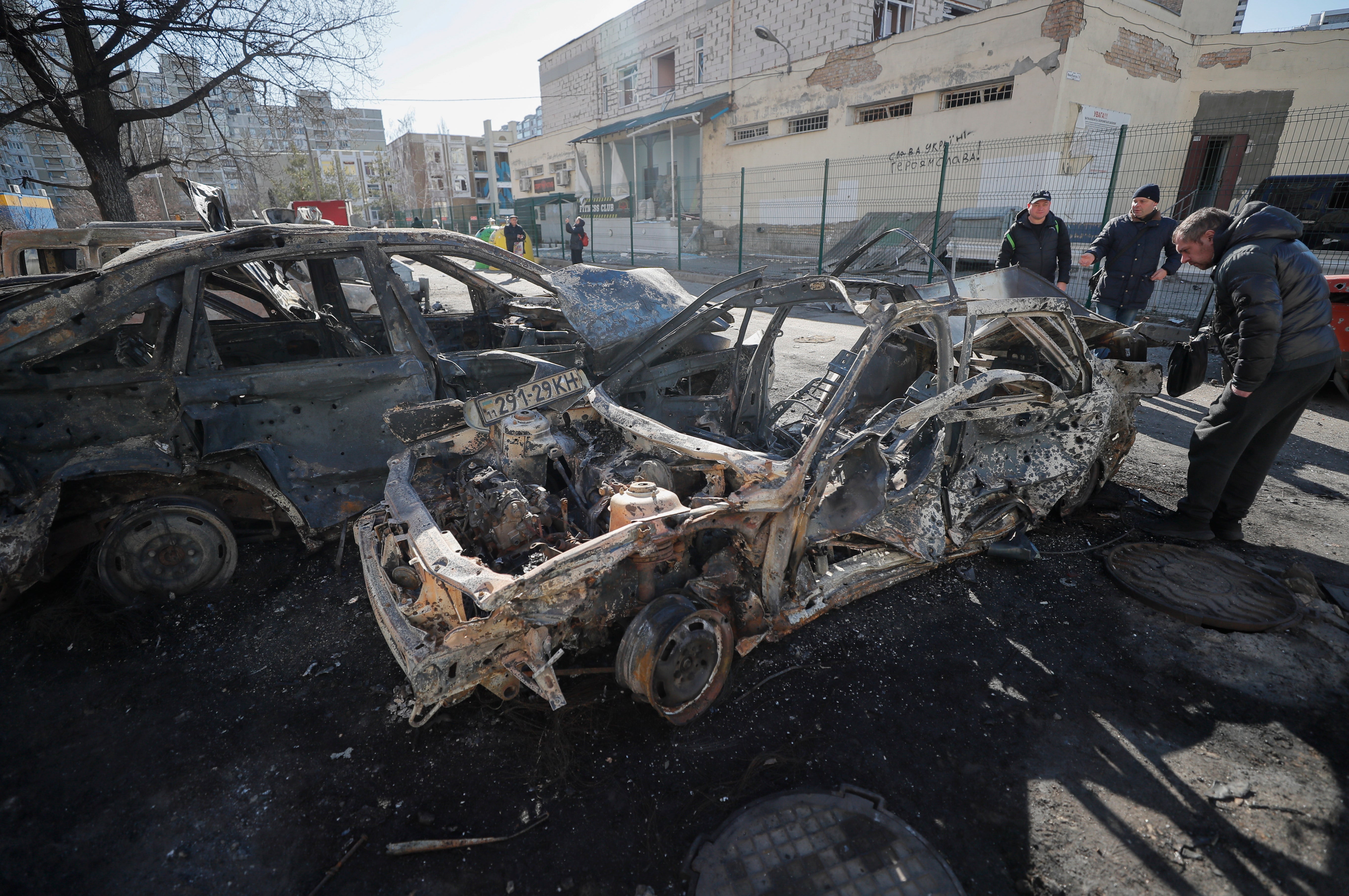 People walk past burned cars a day after a shelling on a residential area in Kyiv