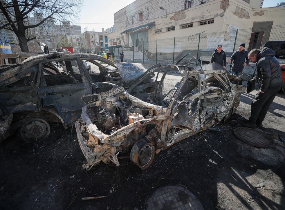 <p>People walk past burned cars a day after a shelling on a residential area in Kyiv</p>