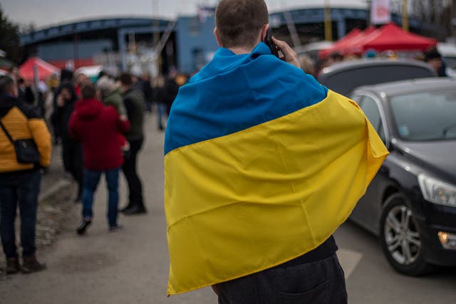 Un hombre envuelto en la bandera ucraniana en el cruce fronterizo con Eslovaquia mientras los refugiados huyen del conflicto.