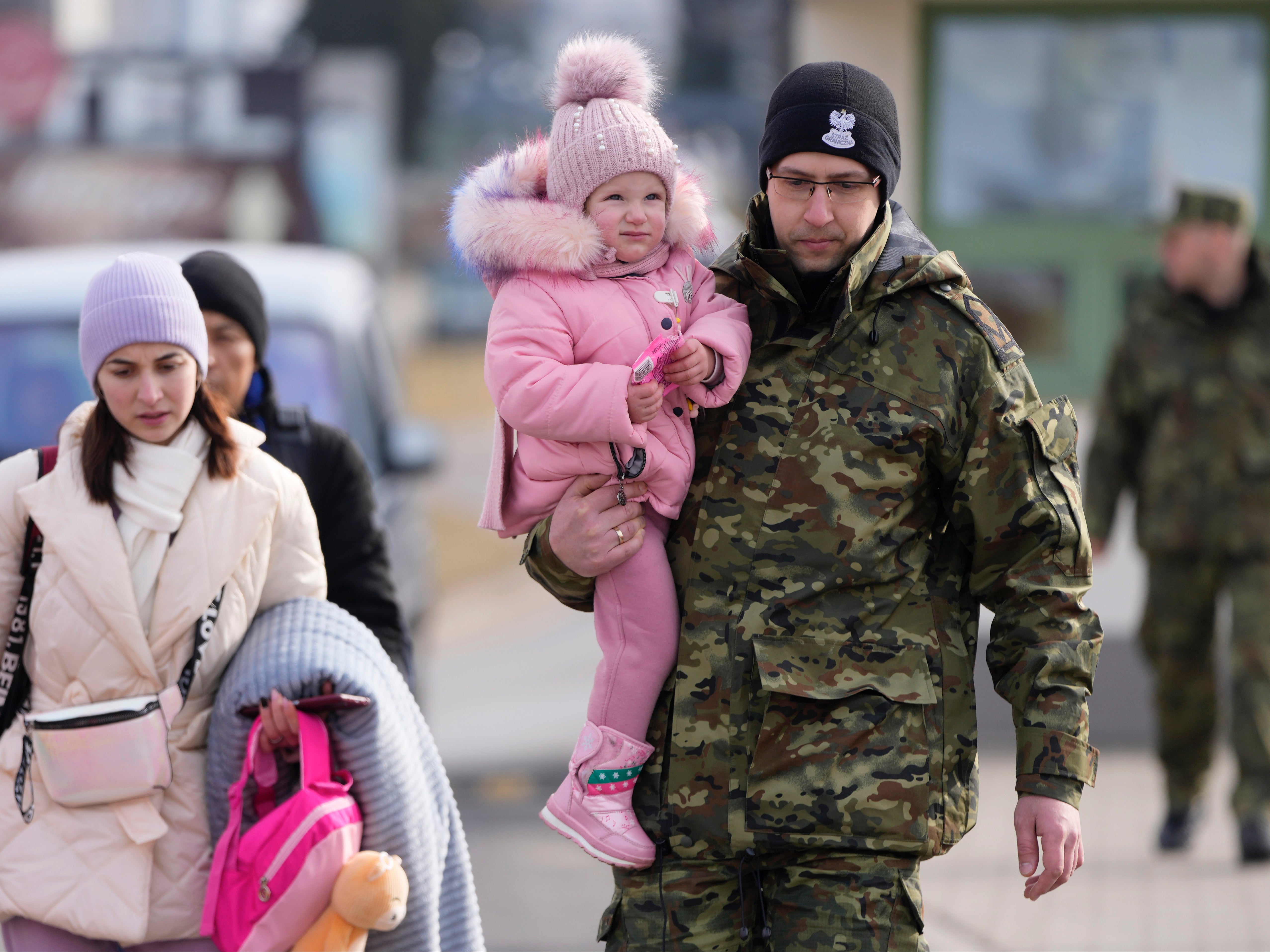 A Polish border guard carries a child as Ukrainians cross into Poland