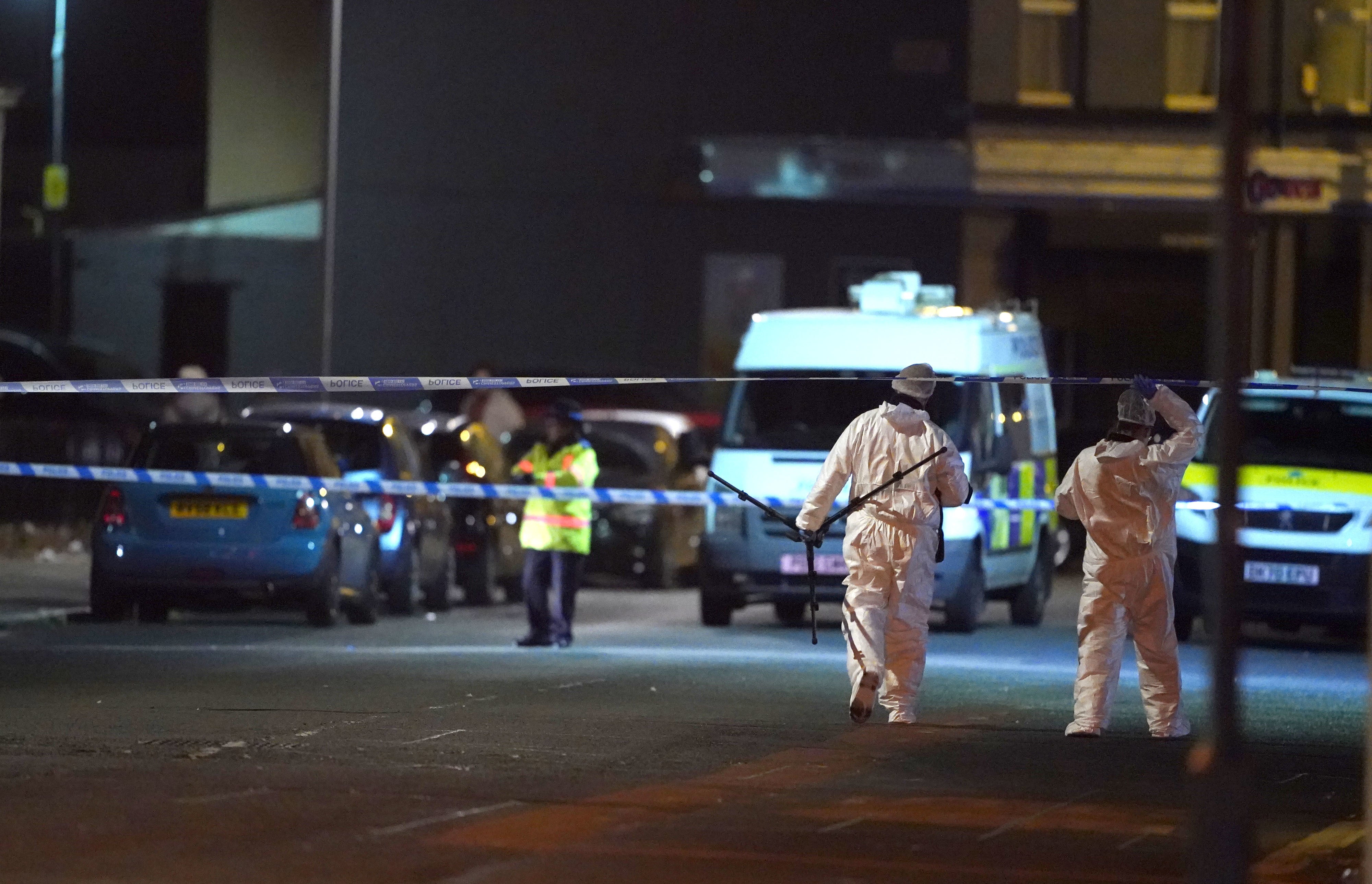 Forensic investigators cross a police cordon by scene of shooting